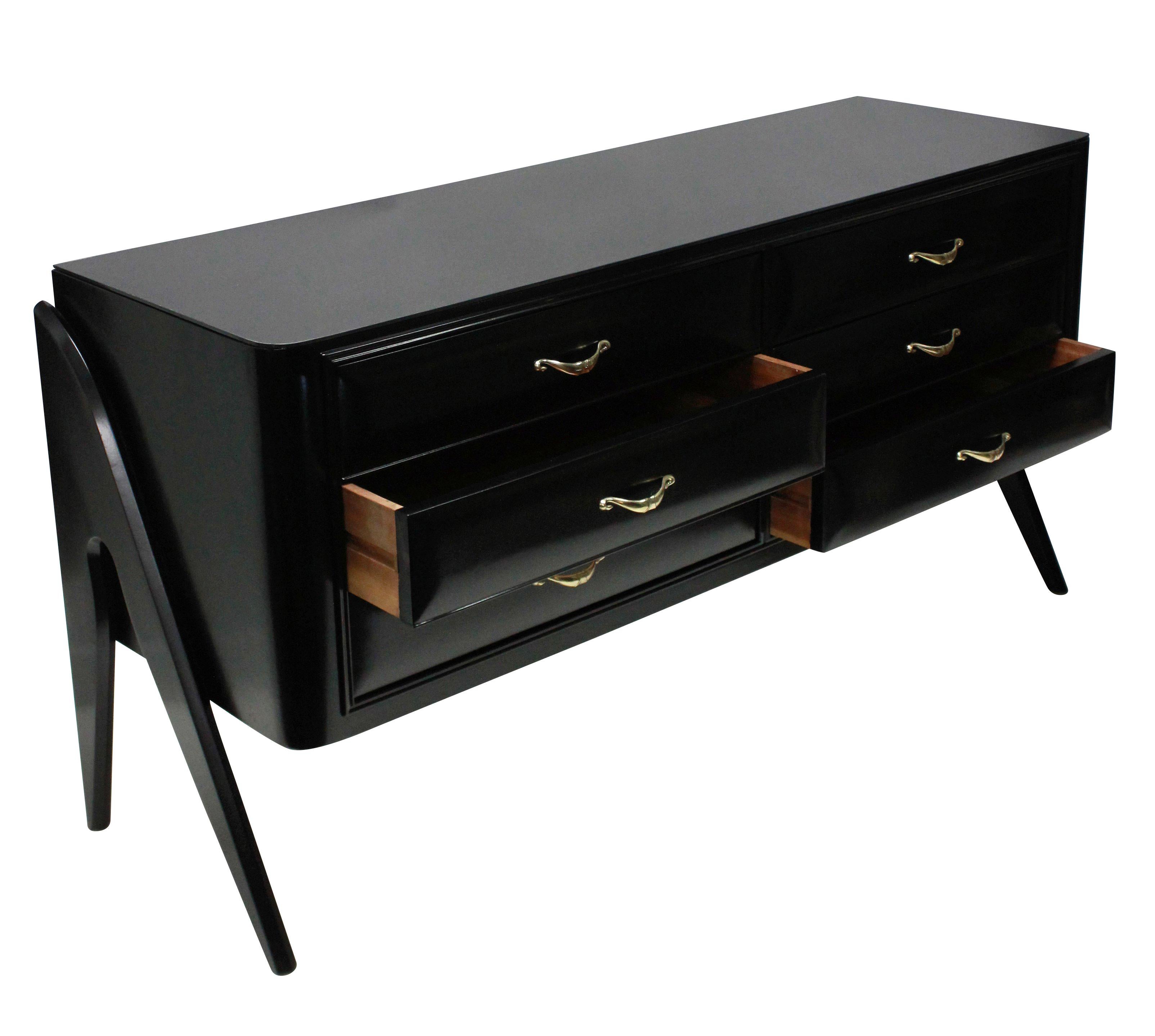 An Italian credenza in black satin finish lacquer, comprising six drawers with fine brass handles. The top of black glass and with architectural side panel legs.