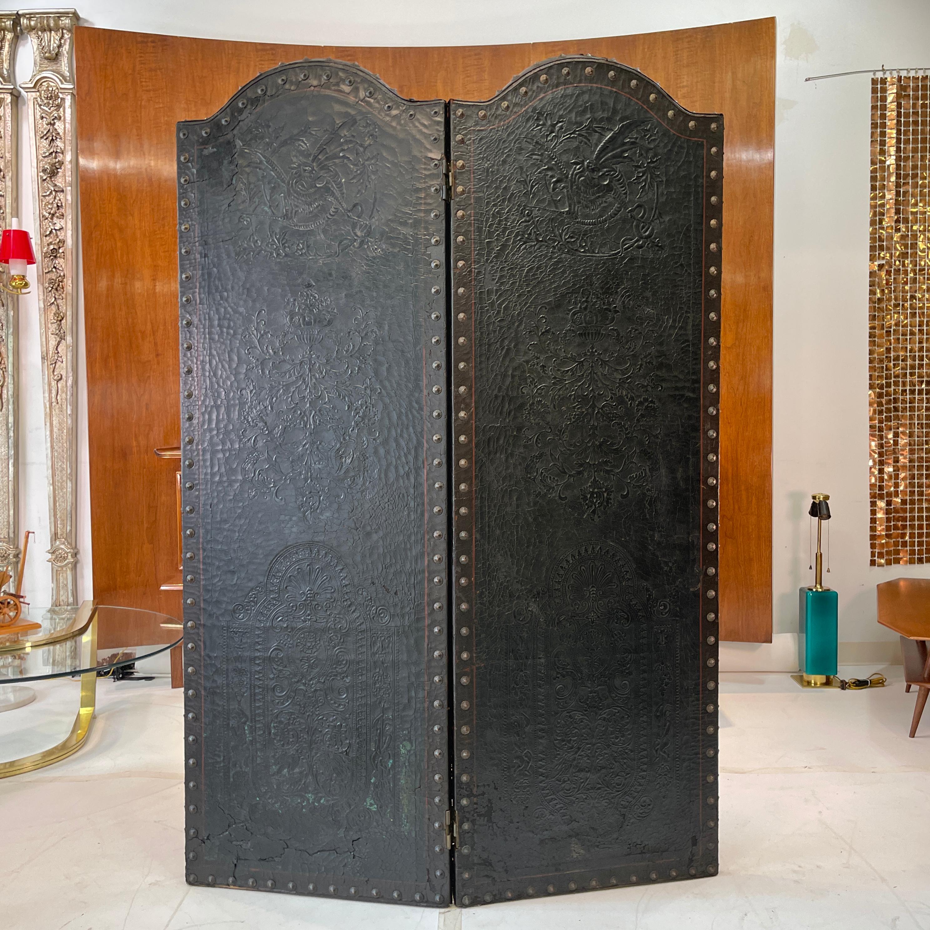 Two panel Italian floor screen (paravent / divisore) room divider in embossed Florentine leather on a hinged wood frame backed with blackened cotton duck canvas embellished with decorative bronzed metal tacks, circa 1928. Overall distressed