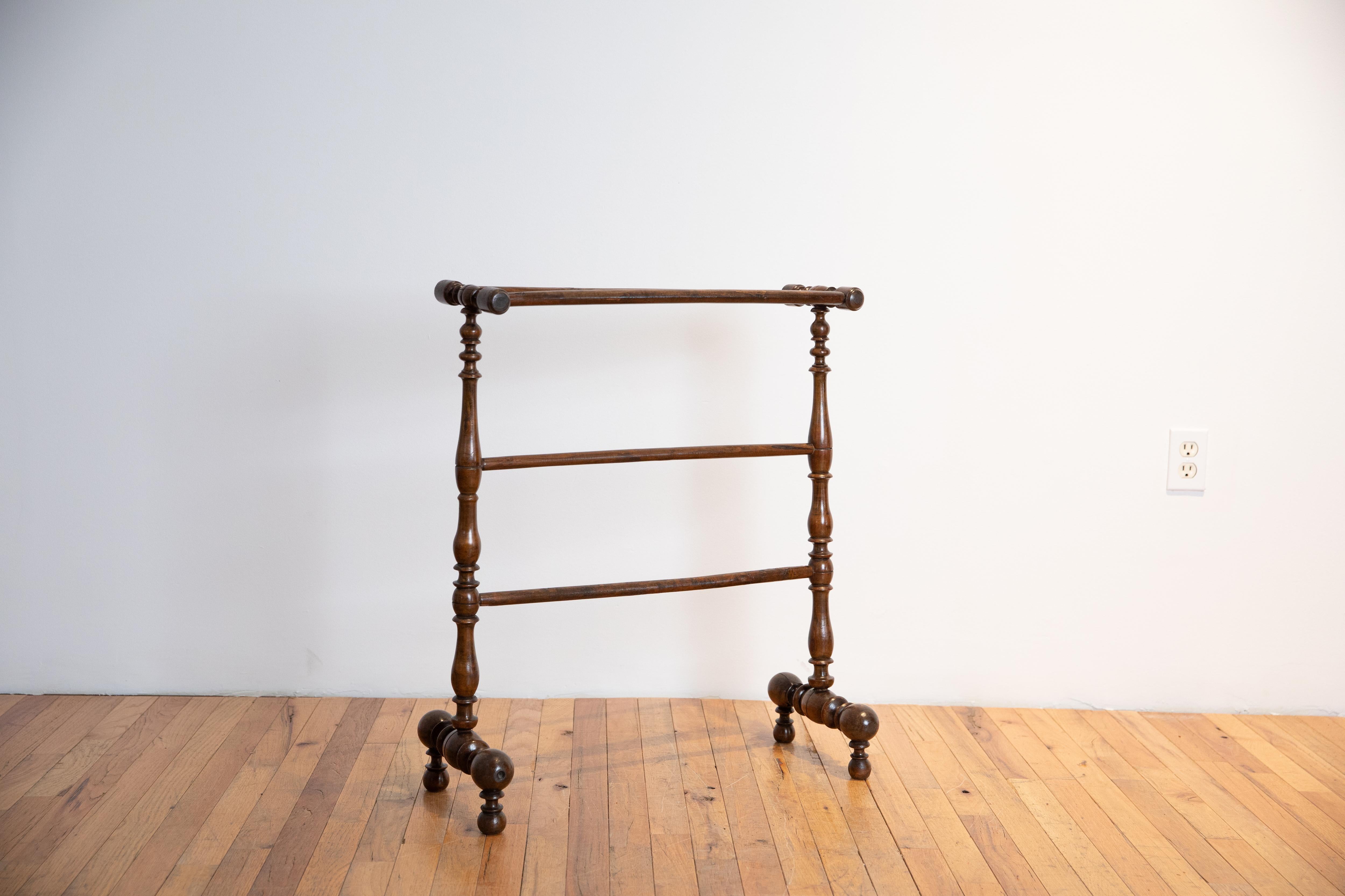 constructed entirely of solid walnut with two top bars supported by turned legs with two more tiers of hanging bars across the middle, the feet are bracket style and are raised on small balls, brass accents throughout