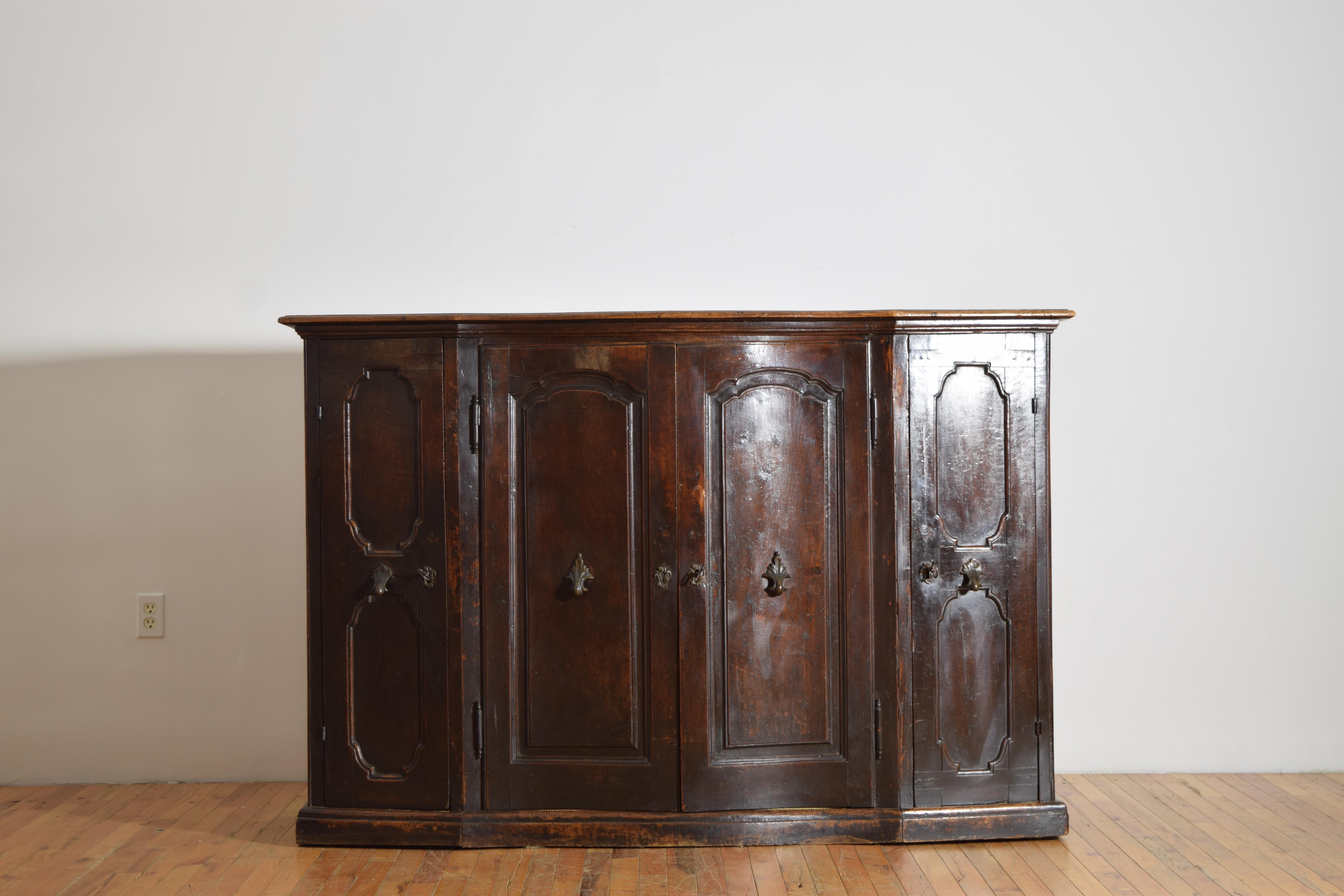 questa importante e rara credenza, costruita interamente in noce, si colloca a cavallo tra i periodi di Luigi XIV e Luigi XV ed è di forma scantonata e serpeggiante, con il piano con bordo modanato che sovrasta una cassa conforme con 4 ante