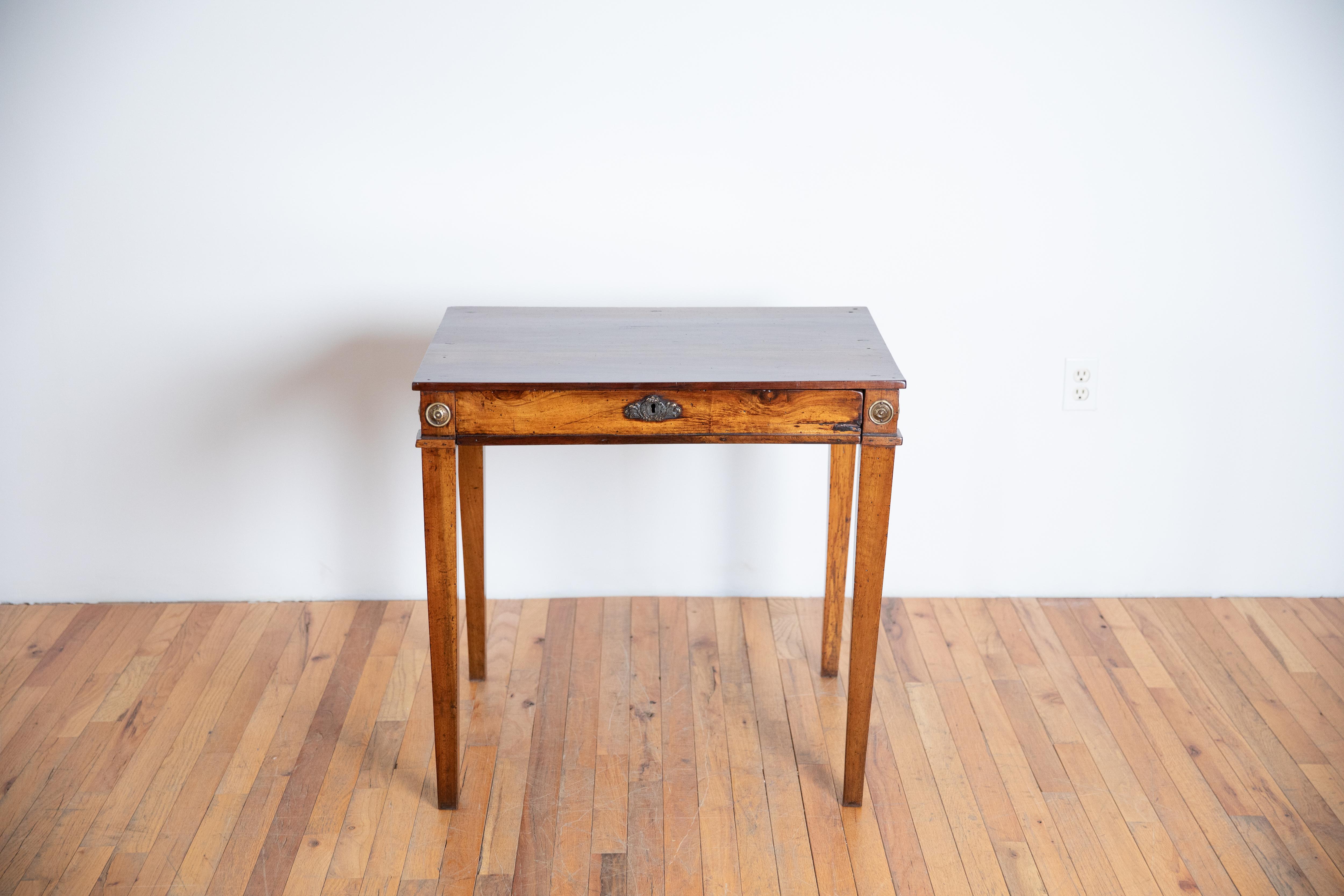 Tiene una encimera rectangular sobre un marco conforme, el faldón con rosetas de latón fundido en las esquinas, y un elaborado escudo de latón fundido, y molduras de latón y alberga un cajón oculto, elevado sobre patas cuadradas ahusadas