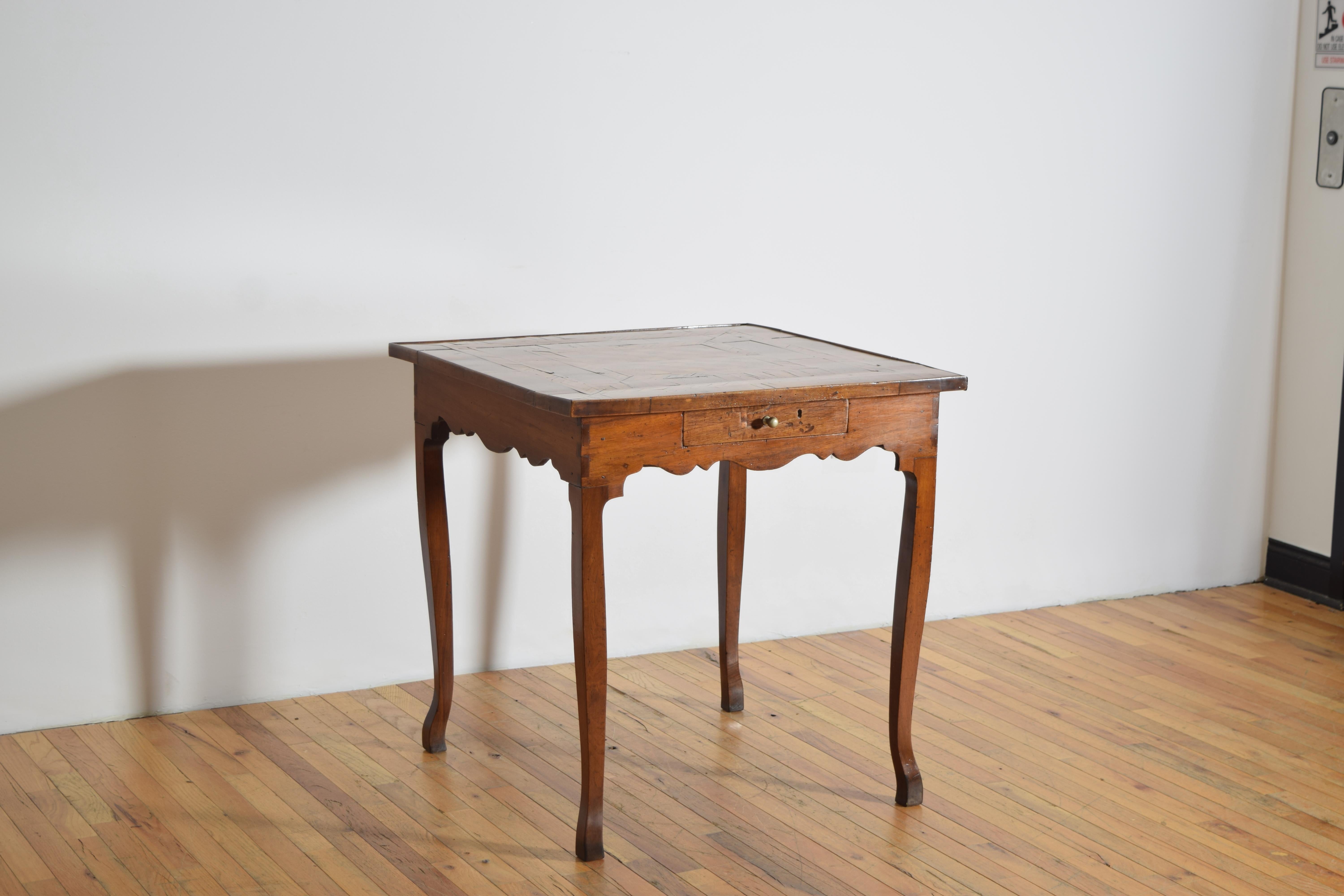 con tablero cuadrado con ligero borde de galería, con superficie de tablero de juego rodeada de una banda de chapa de madera alternada, el faldón perfilado alberga un cajón, elevado sobre patas cabriolé ligeramente ahusadas