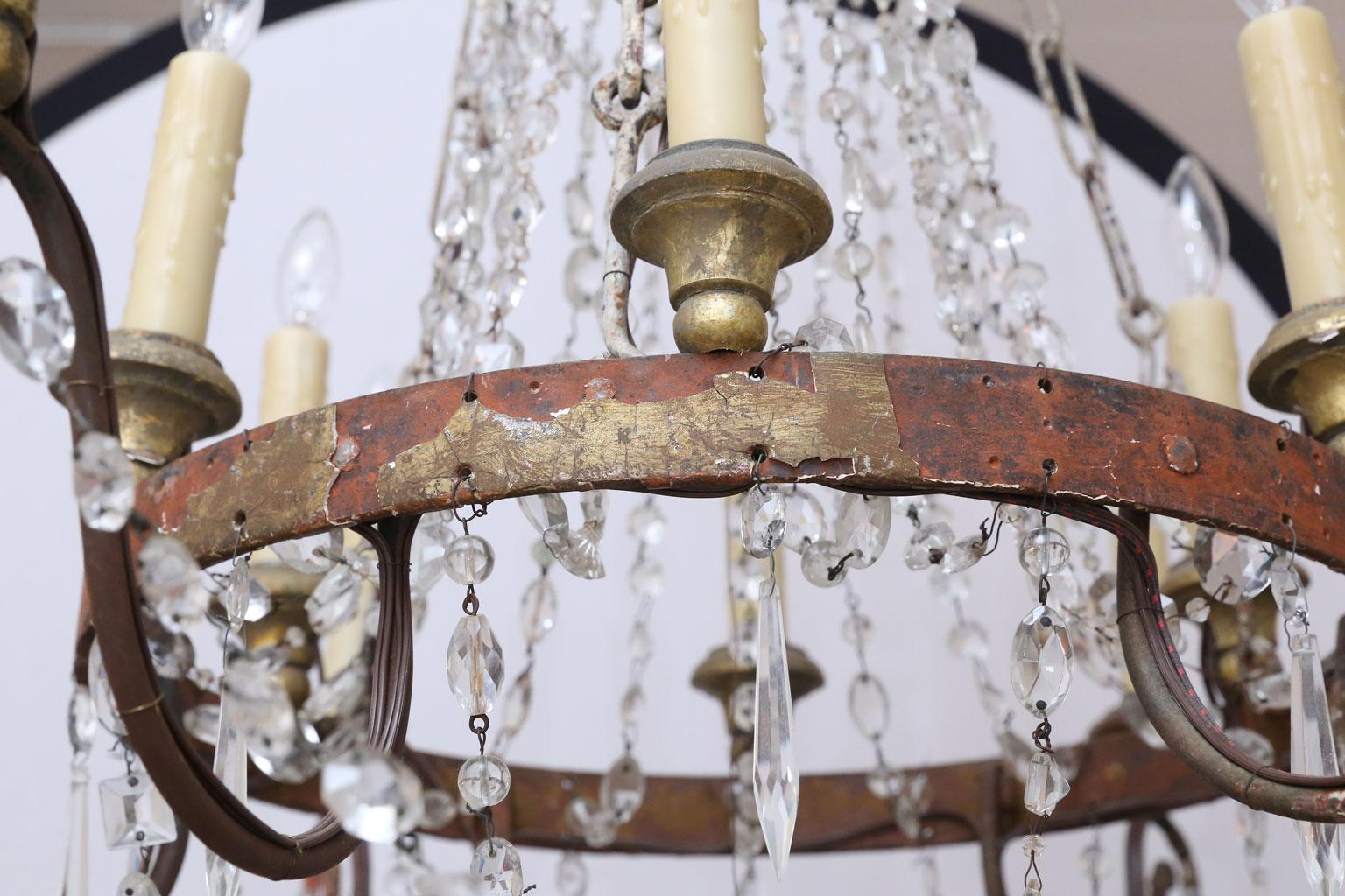 Italian Empire iron and crystal chandelier from Lucca: Red painted forged iron frame and arms with remnants of original gilt and gesso. Two tiers of lights (six upper and six lower) upon turned giltwood bobéches. Decorated with original and later