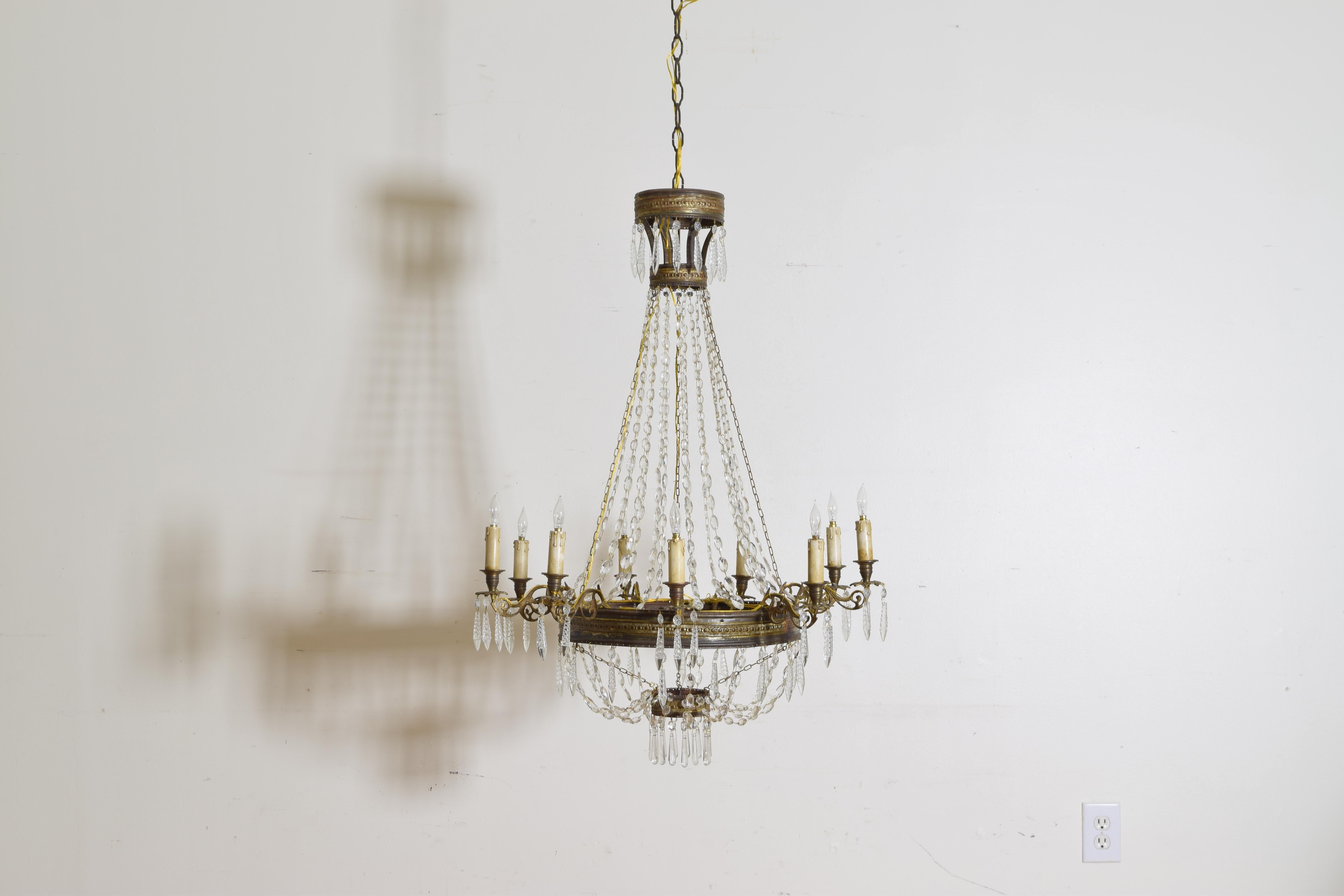 The chandelier of typical basket form with four round sections connected by graduated bead chains, the largest and central ring issuing 9 cast brass arms with bobeches and hanging prisms, the upper and lower rings also with hanging prisms, 19th