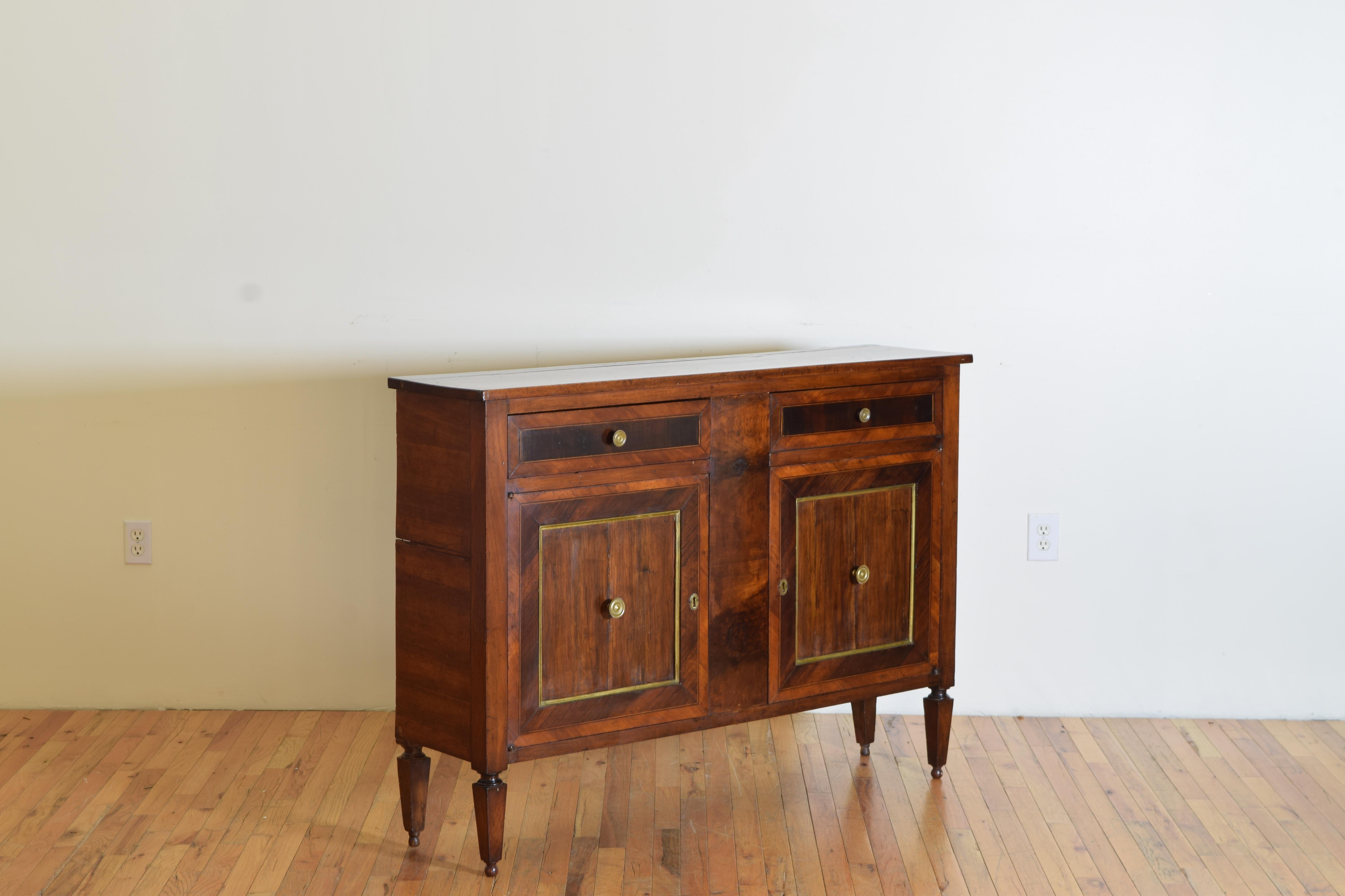 A finely carved handsome credenza with a solid walnut top, veneered walnut sides, banded veneered mahogany inlay on the drawer, and door fronts. The giltwood banded frame the mahogany fronts and brass hardware. The credenza is raised on four