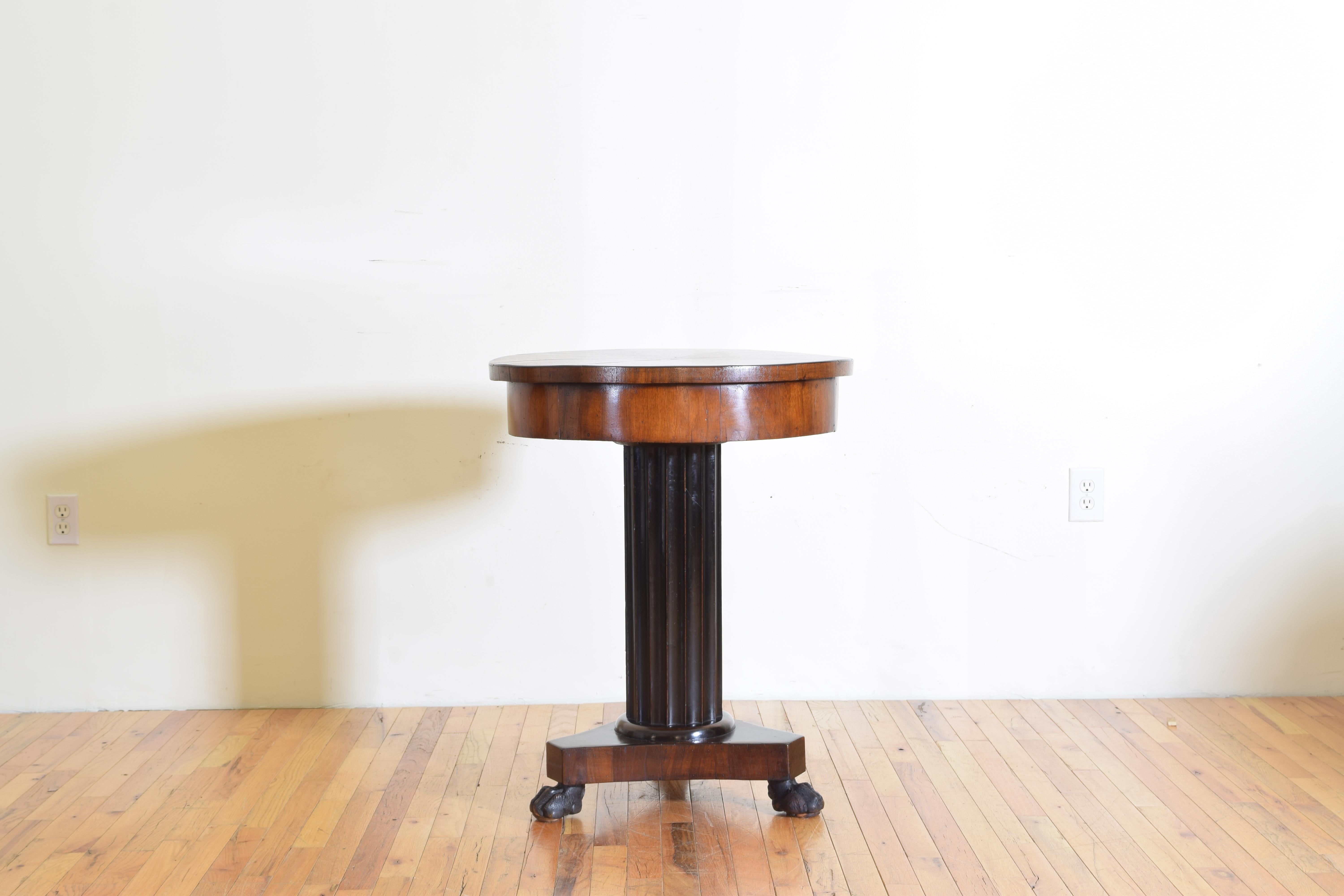 The circular top having pie-shaped veneers and housing one drawer, raised on an ebonized fluted standard above a tripartite base resting on ebonized paw feet, early 19th century.