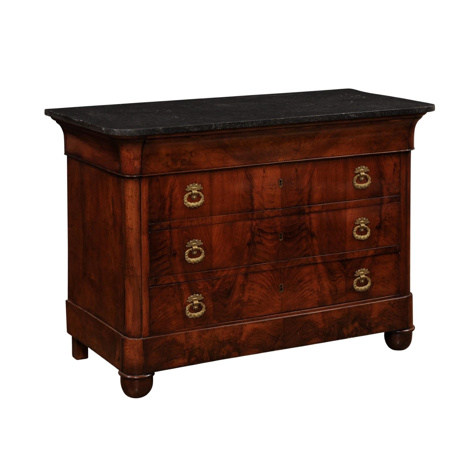 An Italian Empire style walnut commode from circa 1890 with black marble top, four drawers, column shaped side supports and ornate bronze hardware. Step into the grandeur of late 19th-century Italian design with this exquisite Italian Empire style