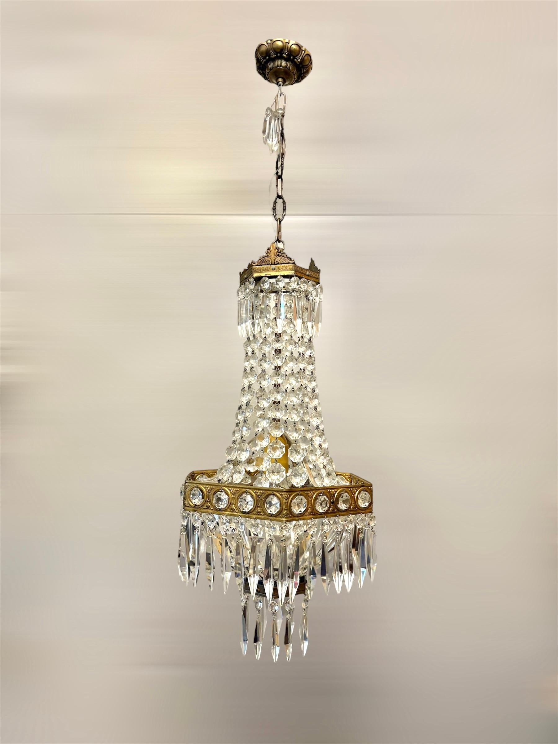 Questo raffinato lampadario italiano degli anni '50 è realizzato in stile Impero, con una struttura in ottone dorato finemente dettagliata e ornata da autentici cristalli di Boemia.

Il design presenta un grazioso corpo affusolato con fili di