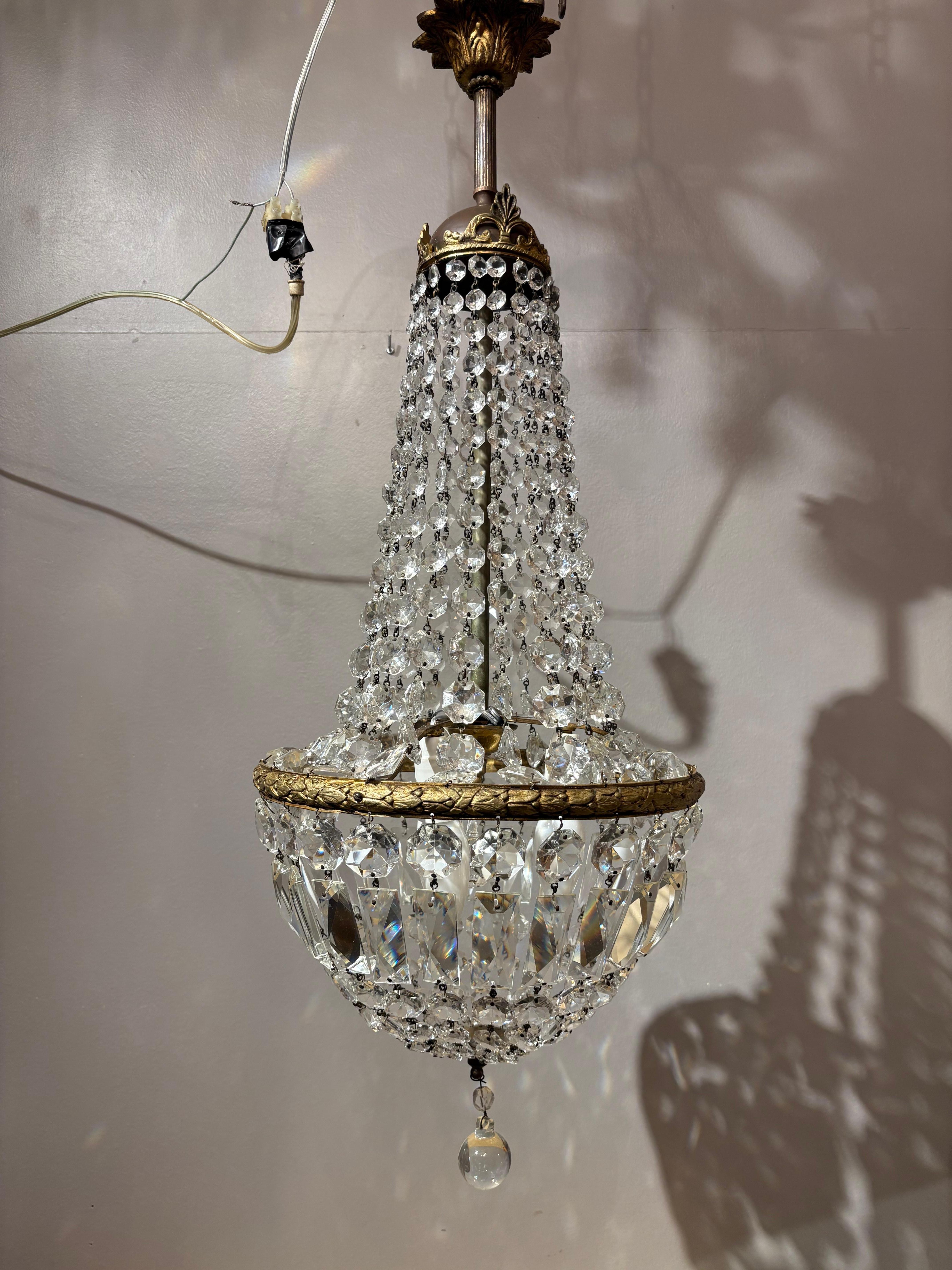 This refined 1950s Italian Empire-style chandelier features a beautifully tapered basket design crafted in gilded brass and adorned with high-quality Bohemian crystal. The upper section is composed of cascading strings of faceted crystals that