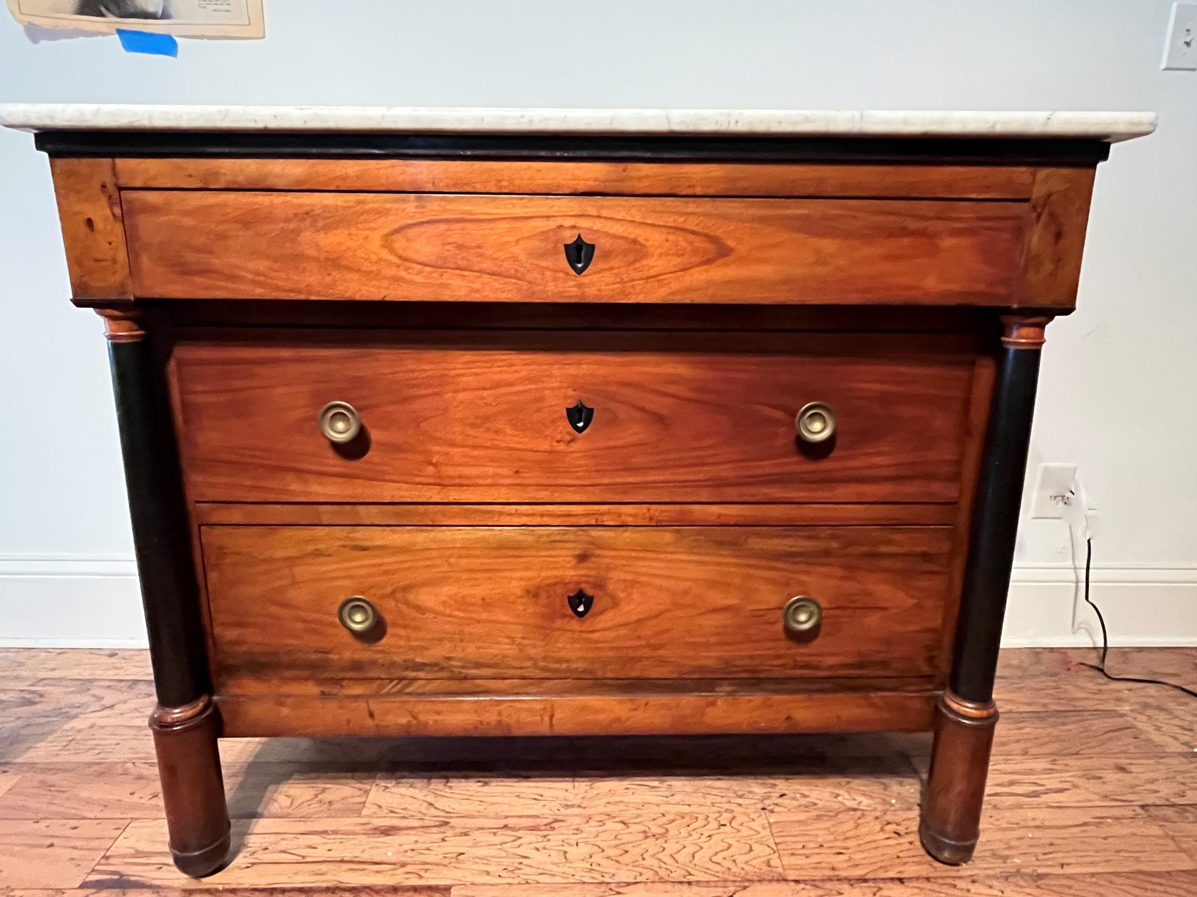 Estate lawyers direct us to sell.  A pretty cherrywood or fruitwood late Empire or Empire style commode flanked with ebonized colonettes. Good provincial feel. The overhanging top drawer separated from the white marble top by an ebonized banding and