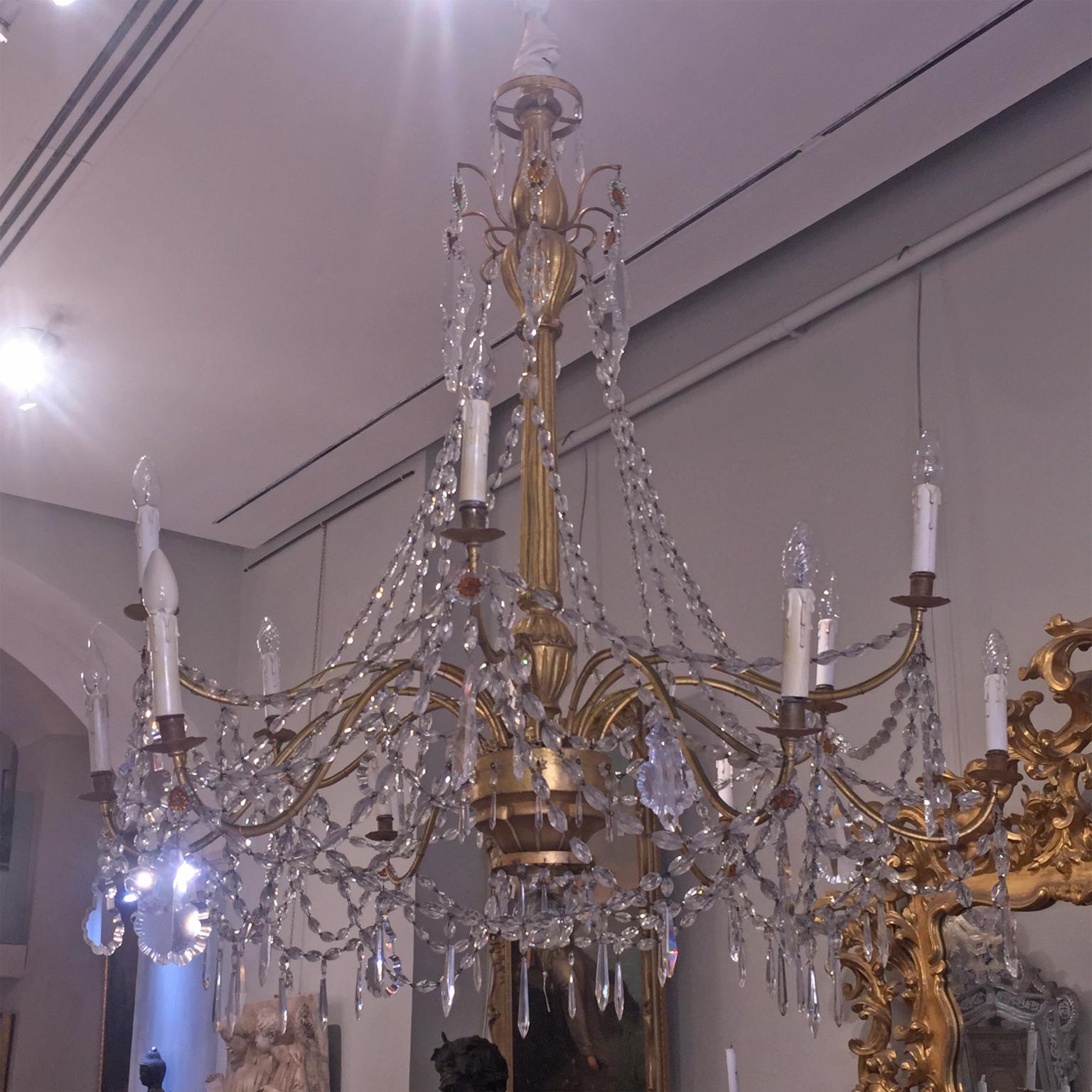 Beautiful Italian chandelier with a central upright in carved wood and gilded with pure gold leaf, with 12 golden wrought iron arms. Finished with ground pendants. Genovese Manufactory of the end of the 18th century. This chandelier is one of a