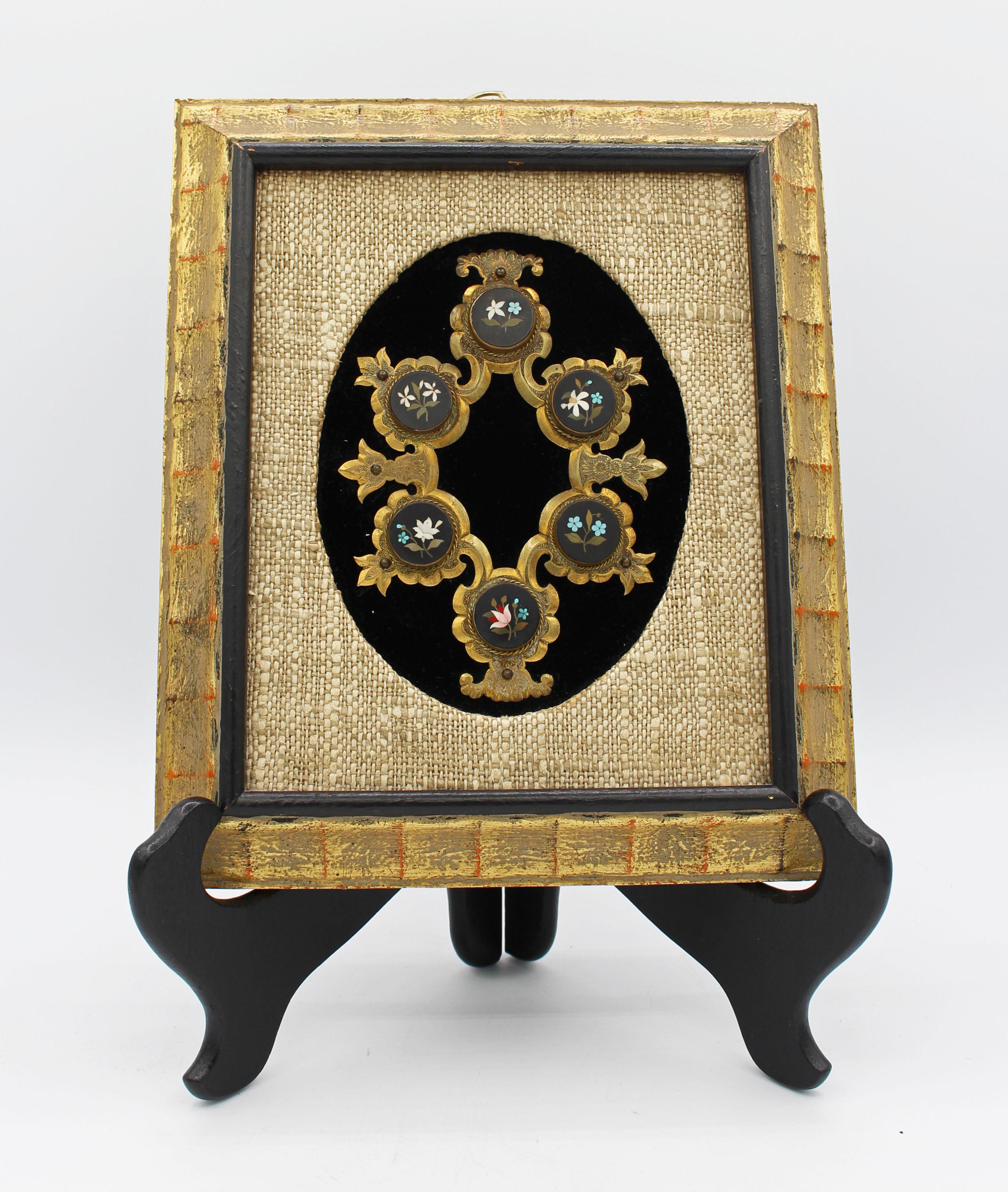Italian, c.1880, engraved gilt brass cartouche set with six floral pietra dura circular medallions, now on black velvet ground with linen matt in rubbed gilt frame. Exquisit workmanshipship. One minute petal lacking in medallion at four o'clock.