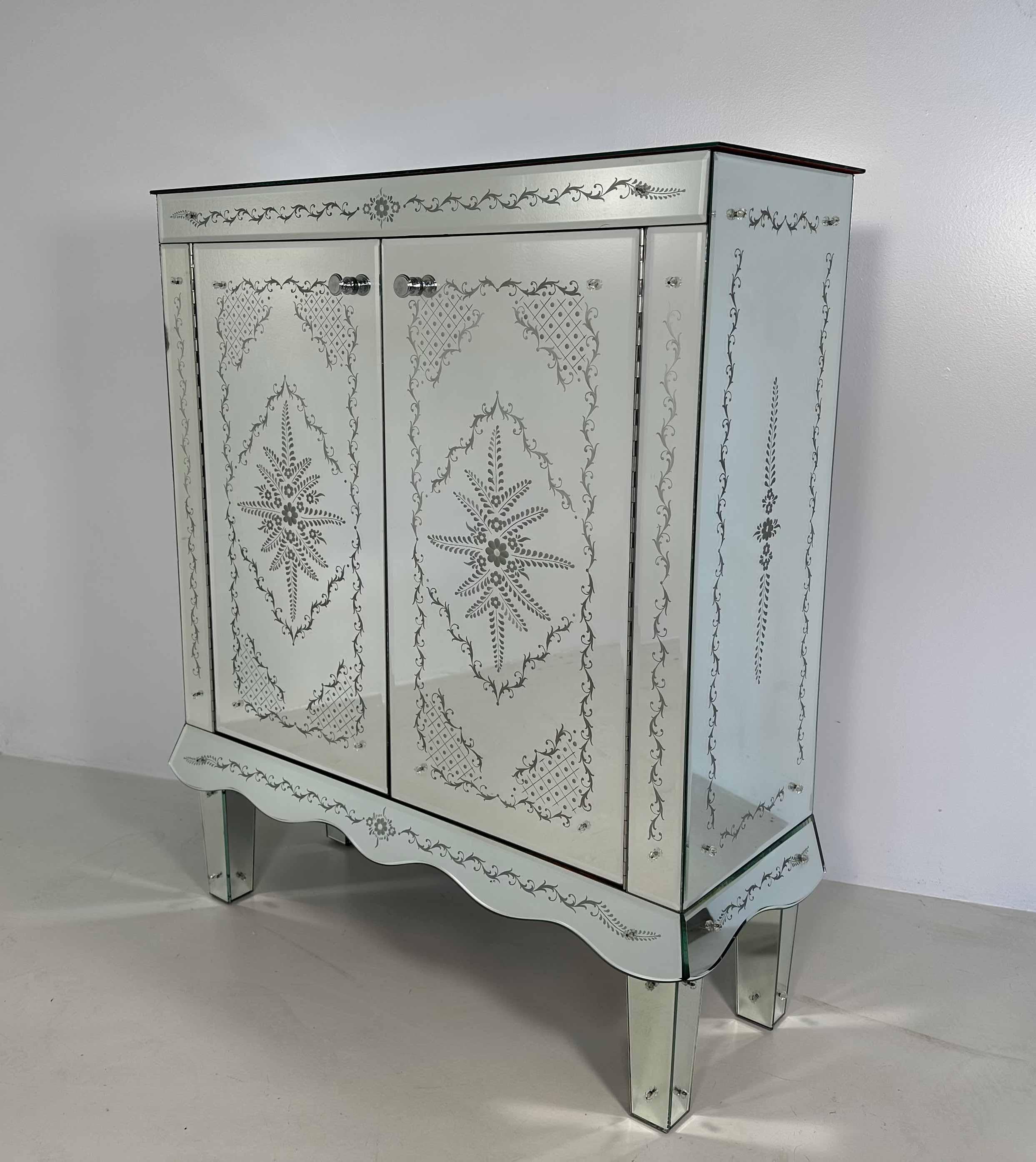 This Art Deco style Cabinet was produced in Italy in the 1980s circa. 
It is completely covered of Murano Glass bevelled panels. The real star of this piece is her majesty the engraving. The patterns on the mirrors, obtained by means of its grinding