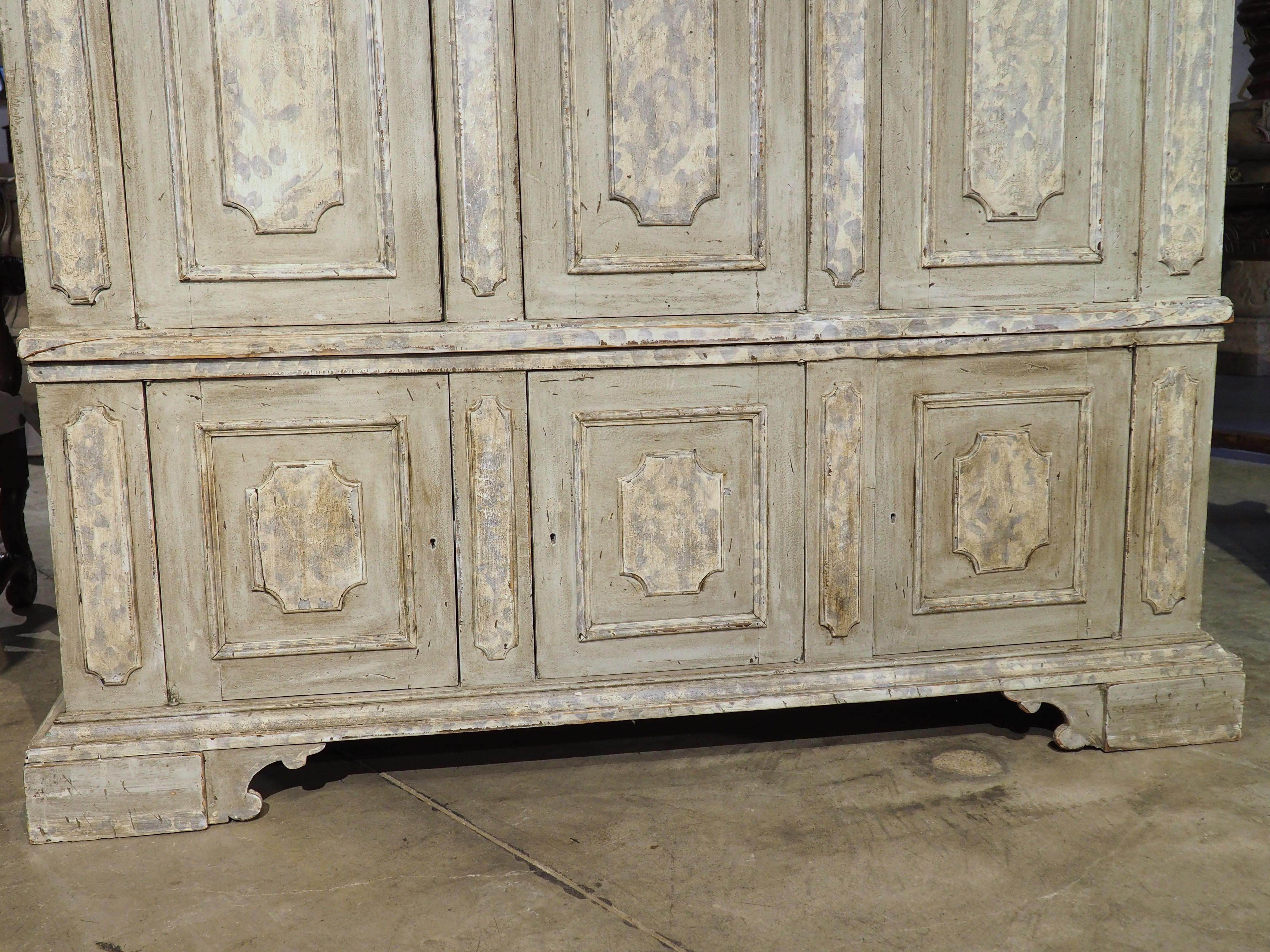 Known as an armadio, this Italian wardrobe has a painted faux finish consisting of cream and blue striations over a gray background. The upper body is topped by a crenelated crown beneath several ogee moldings. All three doors feature rectangular