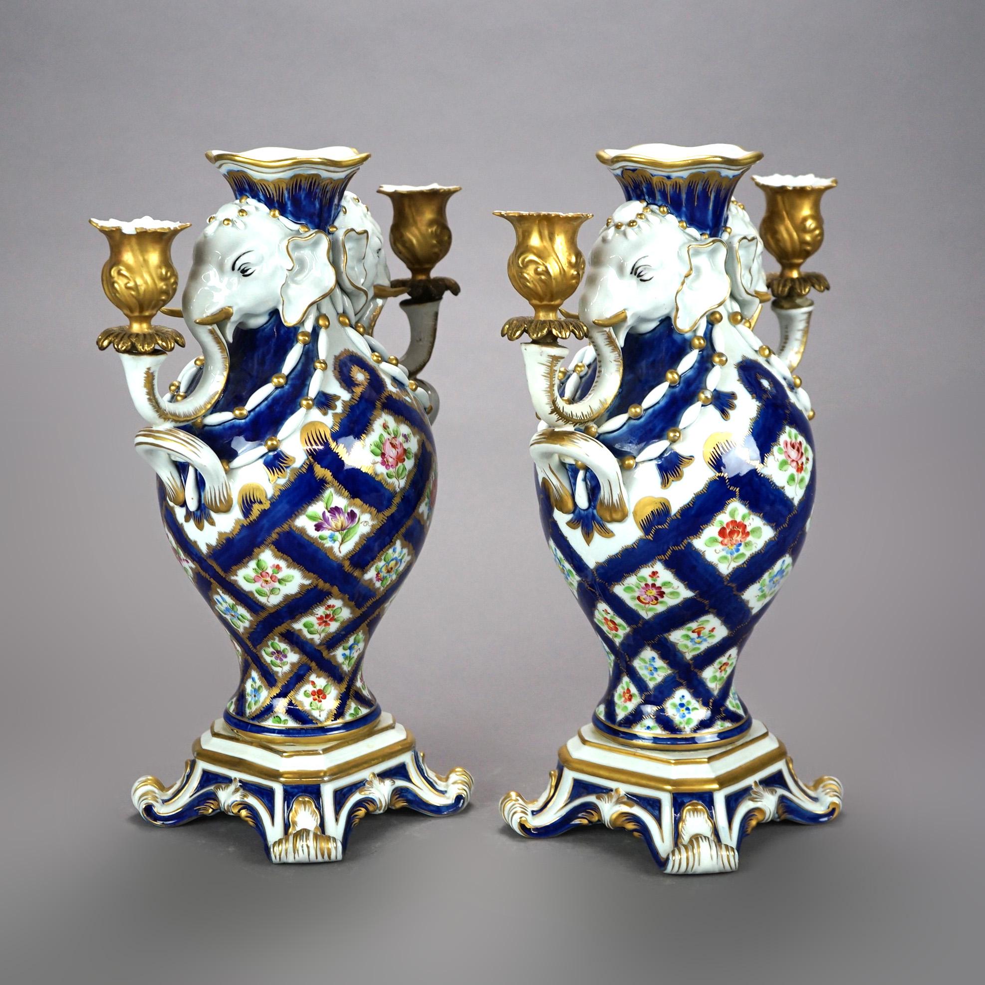 An antique pair of figural Italian candelabra urns offer porcelain construction with cobalt lattice pattern with flowers, flanking elephant candle holders, raised on footed base, gilt highlights throughout, maker mark on base 