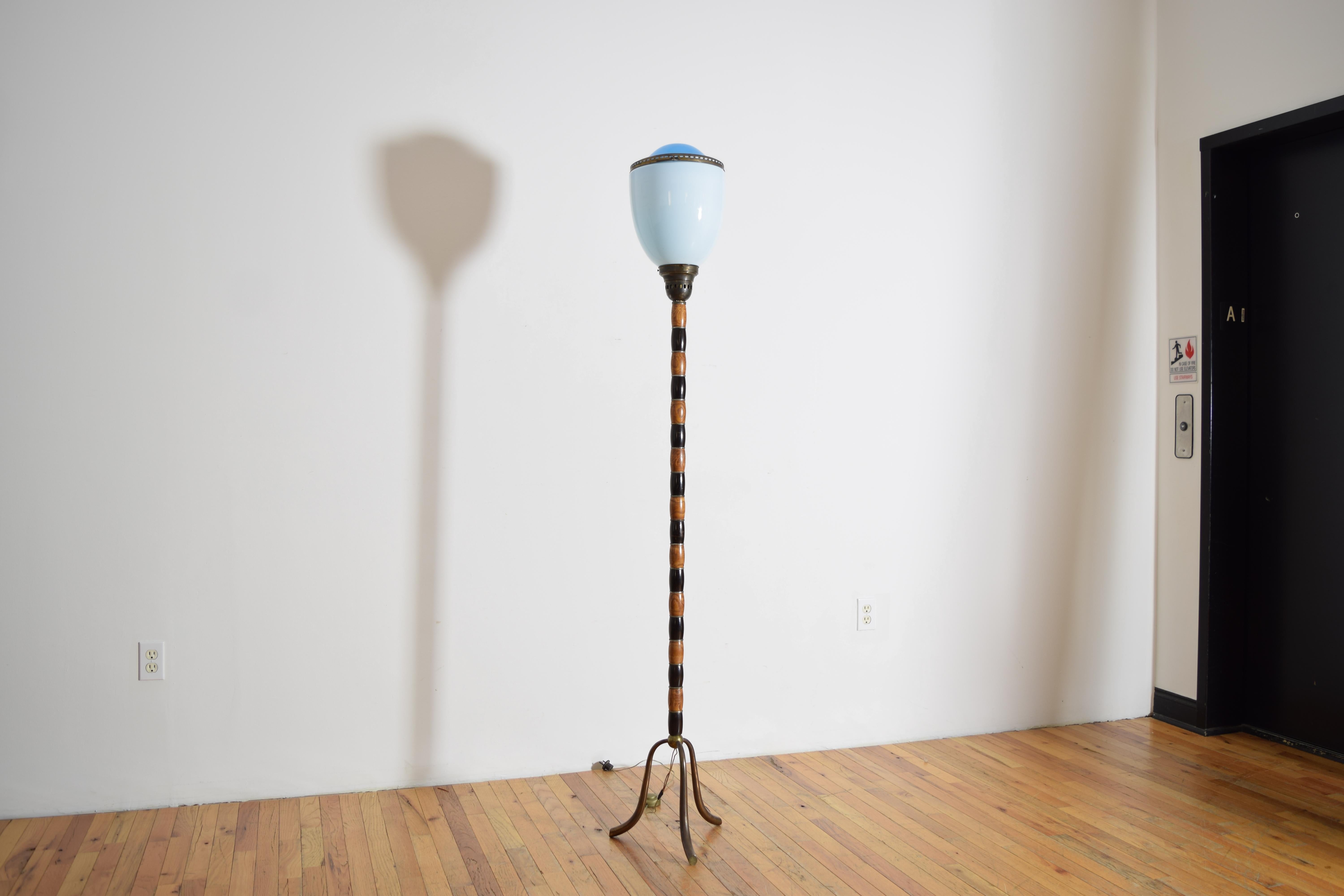 having a unique two piece shade of blue glass and opaque glass fitted together with a brass ring, the shade resting atop a standard of alternating fir and ebonized wood raised on a tripartite brass base