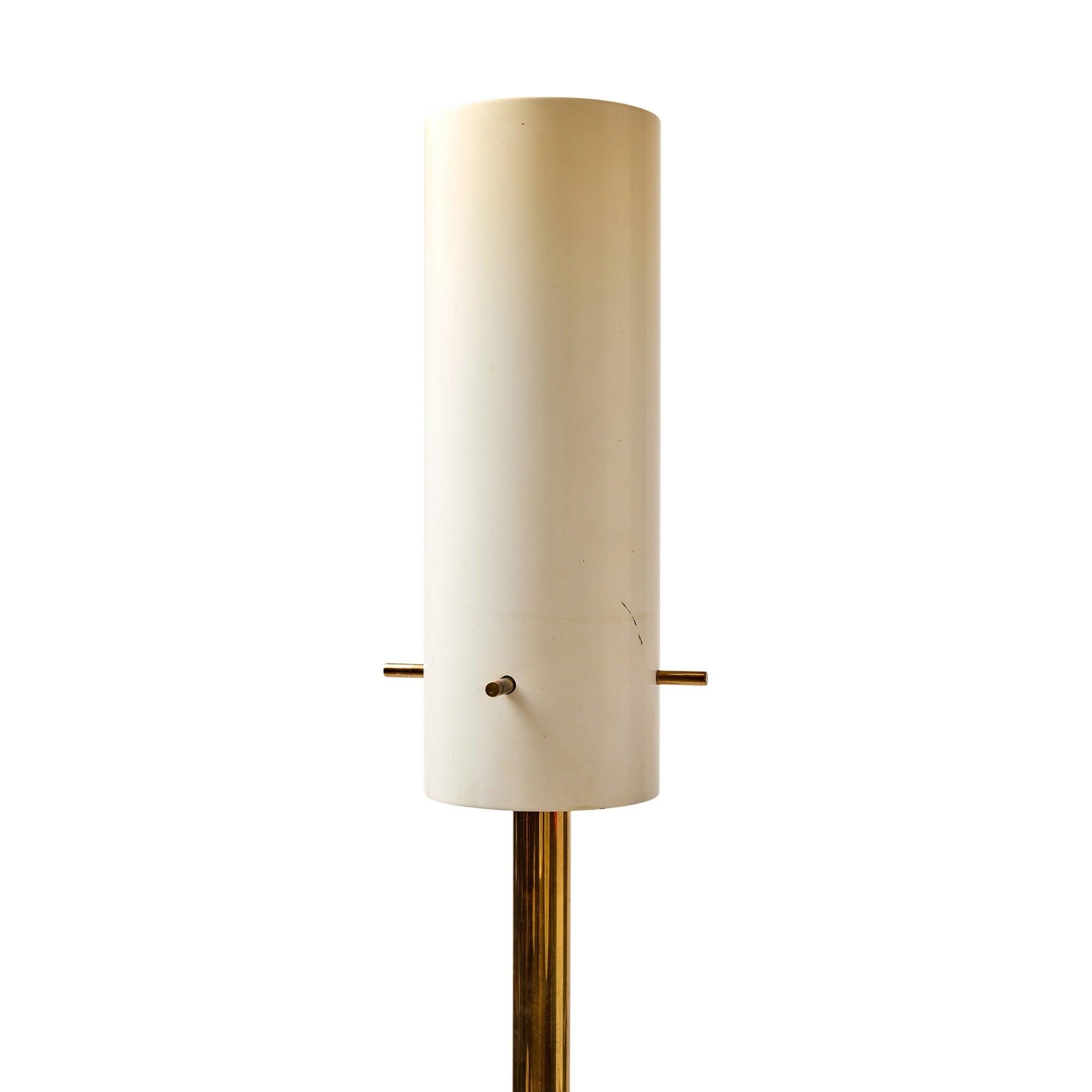 A sleek and minimalist Italian torchiÃ¨re with a brass base and stem, and a lacquered cylindrical shade held by threaded brass rods.