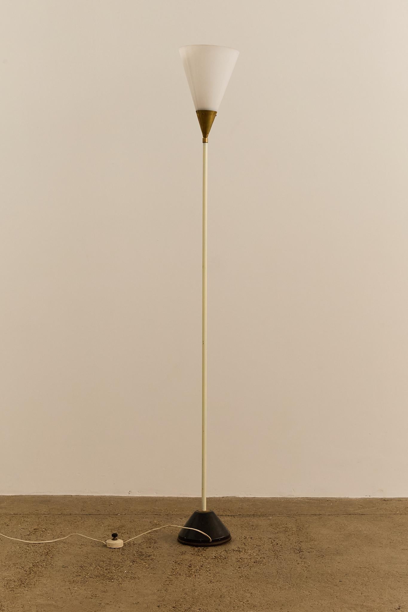 Elegante lampada da terra italiana degli anni '50 con paralume conico in vetro opalino montato su un sottile stelo in metallo verniciato. Il paralume è impreziosito da un collare in ottone, mentre la lampada poggia su una base in metallo nero