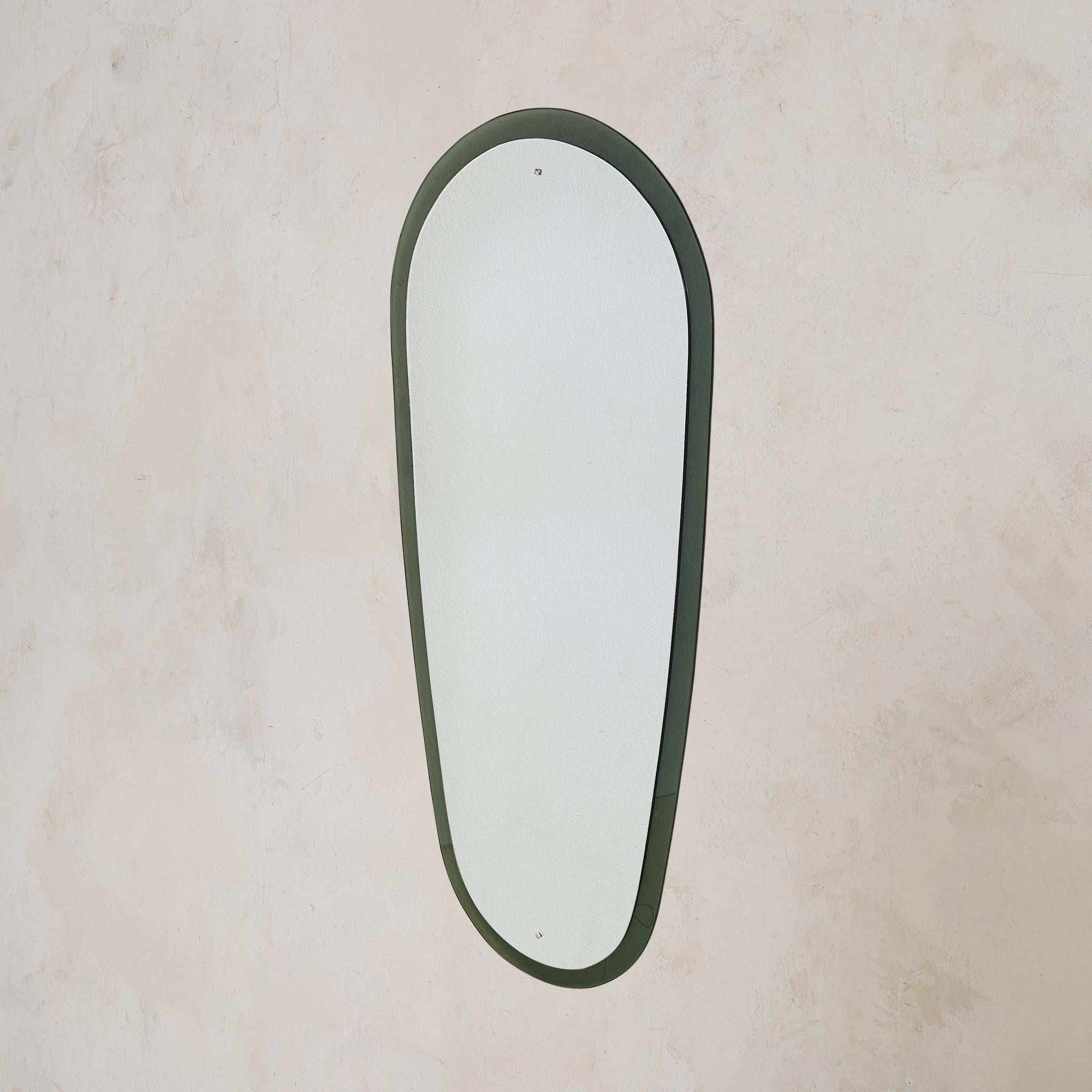 A 1960s Italian wall mirror rendered in smoked glass. The floor-length silhouette stretches over five feet tall, its elongated frame gently rounded at the top and tapering to a soft curve below. Thick, smoky glass borders the mirror plate, catching