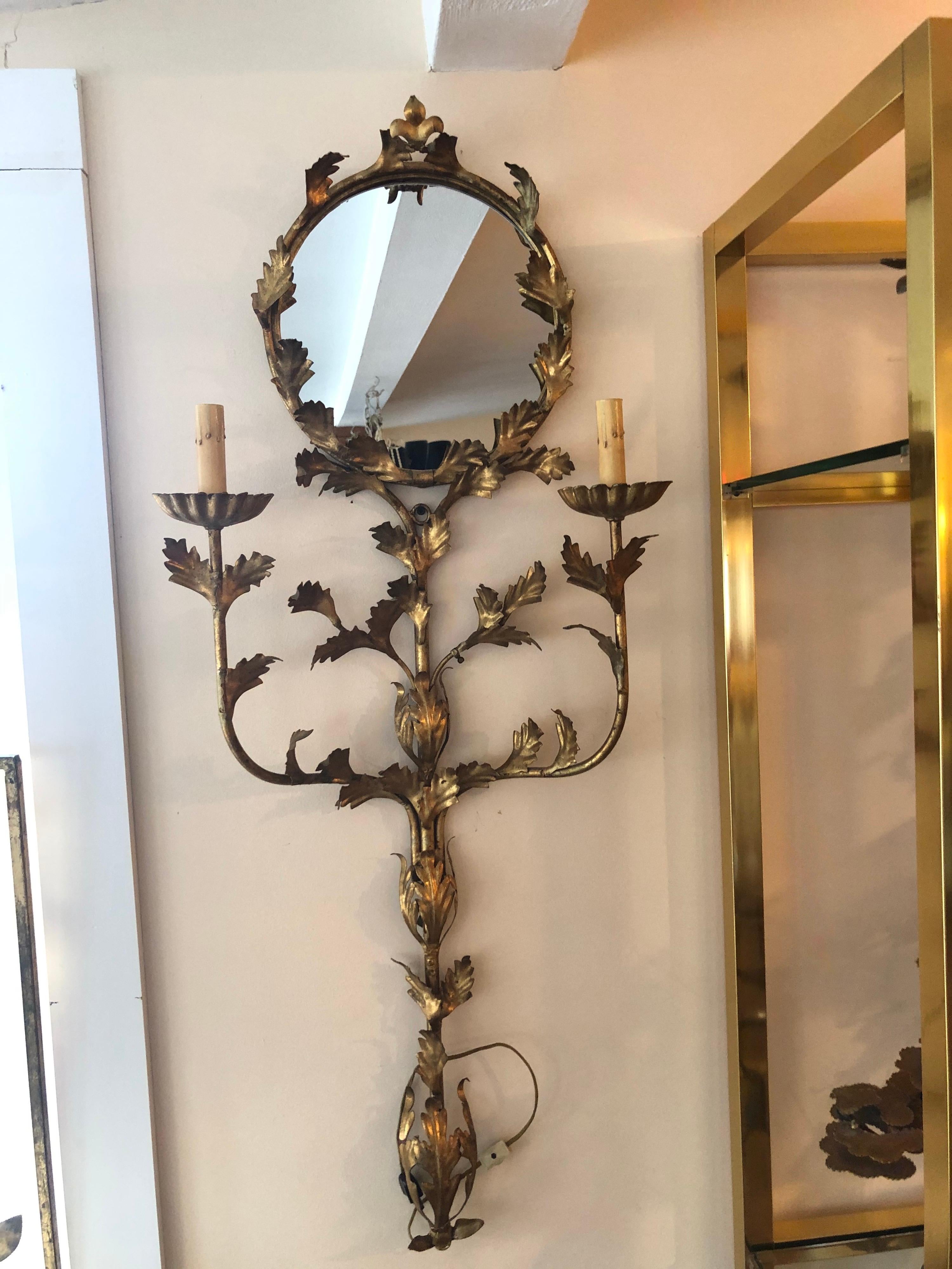 Italian floral gilt iron mirrored wall sconce. Unique, one of a kind, floral wall sconce. Circular mirror in the center surrounded by gilt iron leaves. Electrified with two candle light arms flanking the mirror. Plug in cord for wall outlet but