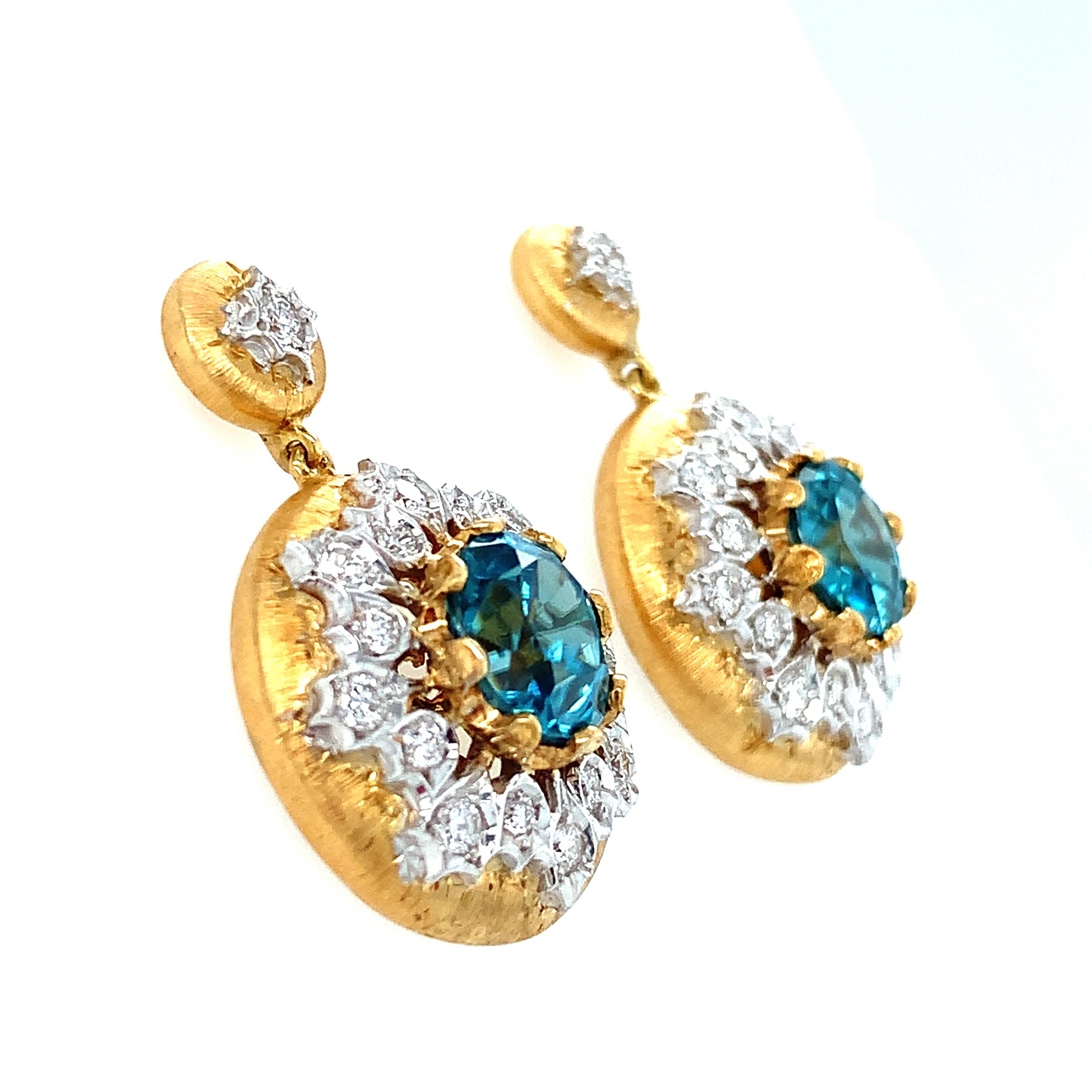 These stunning 18k yellow and white gold drop earrings highlight the natural brilliance of precious blue zircon. Shimmering diamonds radiate from the peacock blue centers, creating exquisite frames that complement the beautiful dispersion enjoyed by