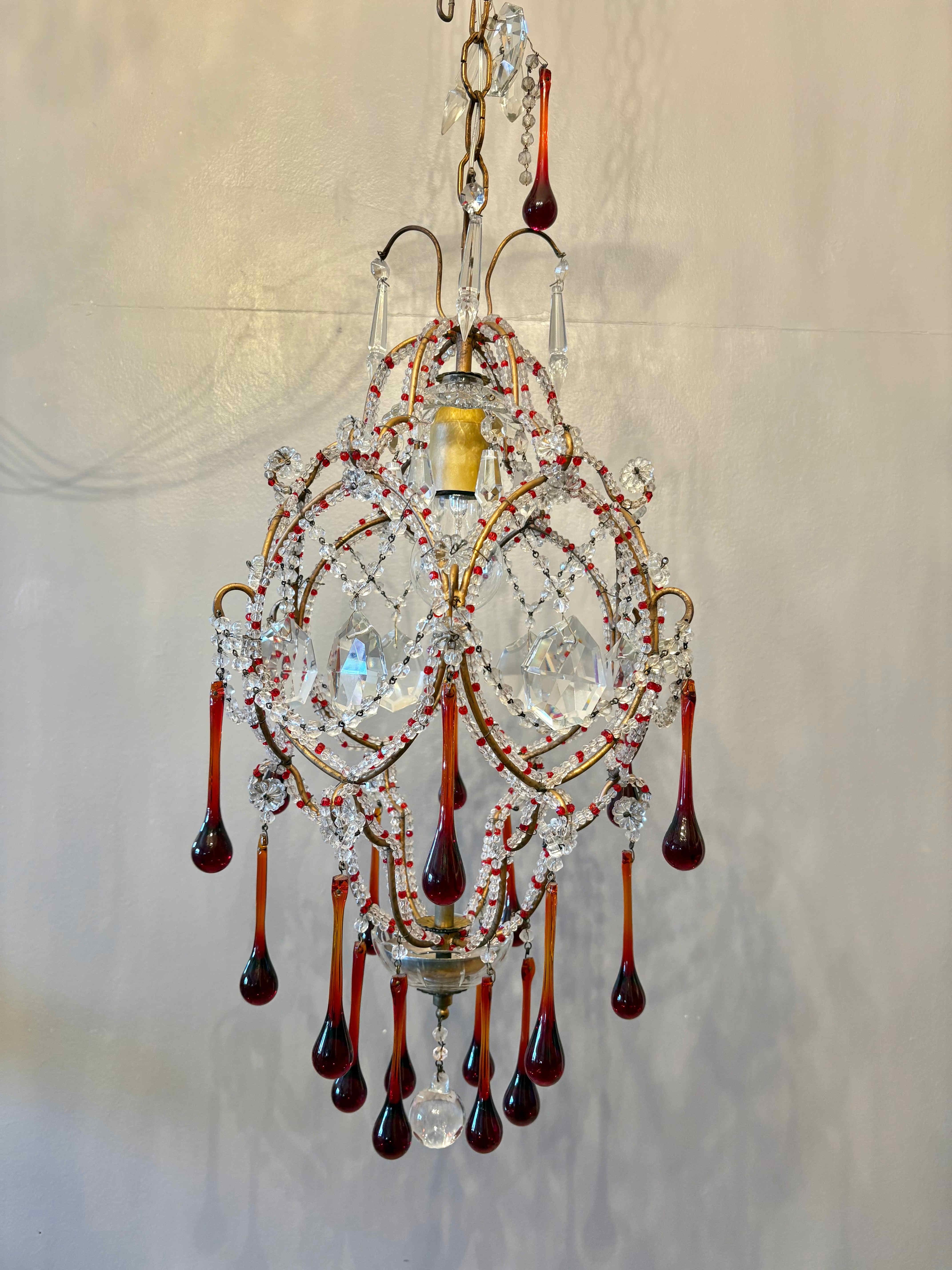 Elegante lampadario Florentine della metà del secolo scorso con struttura in metallo dorato curvato dalla caratteristica forma a gabbia di uccello, riccamente ornato da catene di cristalli trasparenti intervallate da piccole perline rosse che ne