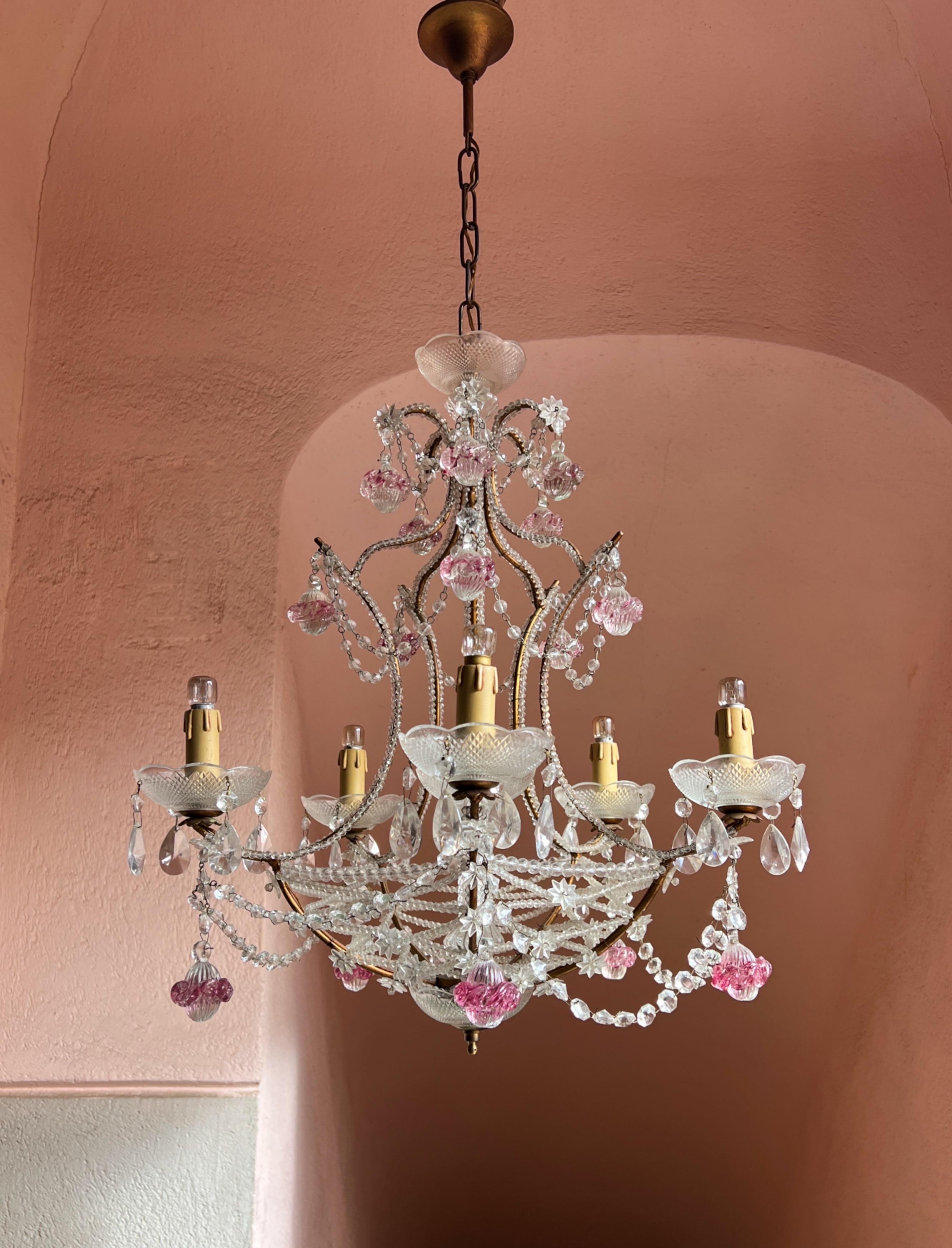 Squisito lampadario italiano Florentine, ornato da delicate fasce di cristallo e gocce di vetro rosa di Murano. Con cinque bracci, ognuno dei quali ospita una lampadina, questo lampadario irradia una luce morbida e invitante.

Perfetto per
