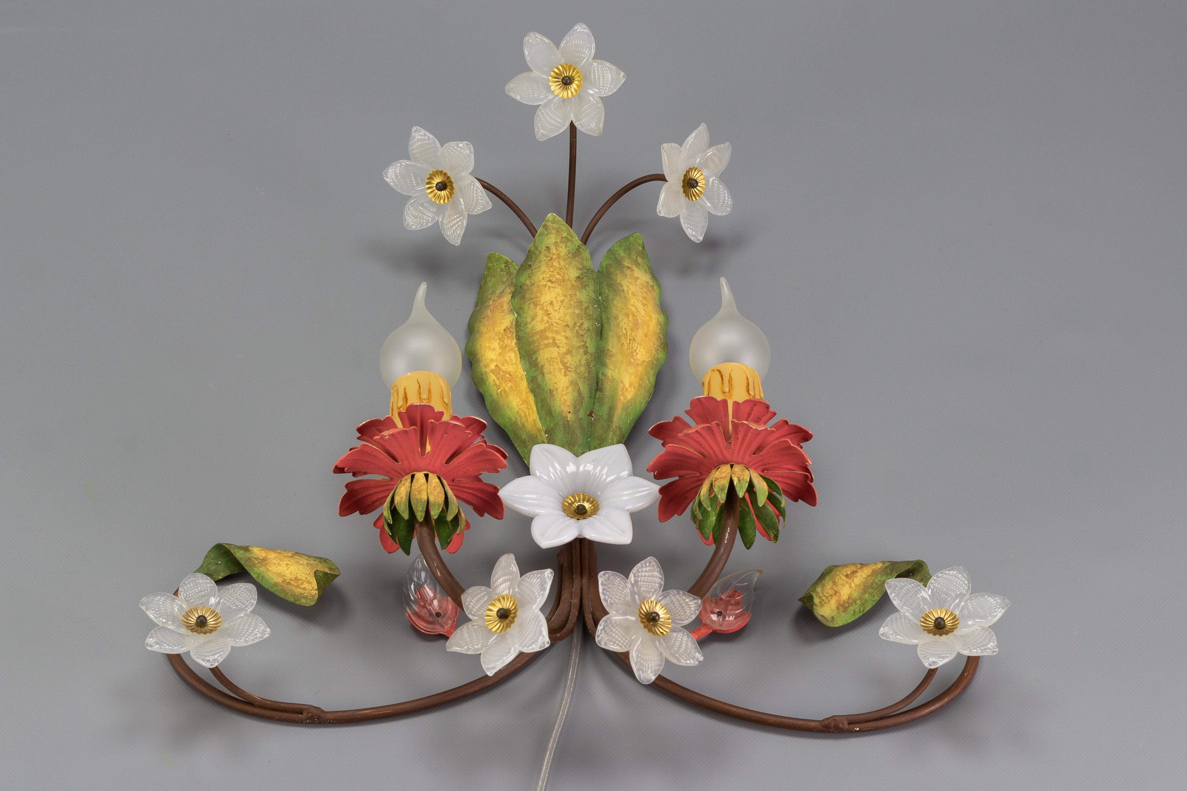 An absolutely adorable Italian Florentine sconce made of metal and glass in the 1970s. This stunning Hollywood Regency style wall sconce features three large metal leaves in green and yellow and is adorned with eight white glass flowers and two