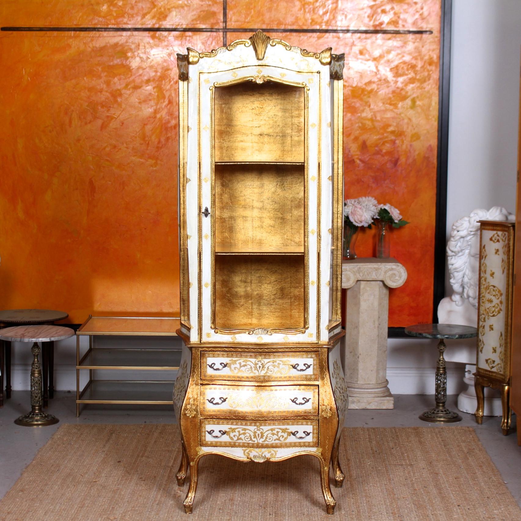 An outstanding Italian display cabinet on chest.

Boasting superb gold gilded detailing and hand painted finish.

The upper section with moulded cornice and shell carved motifs above a glazed paneled door enclosed gilded interior and shelving.