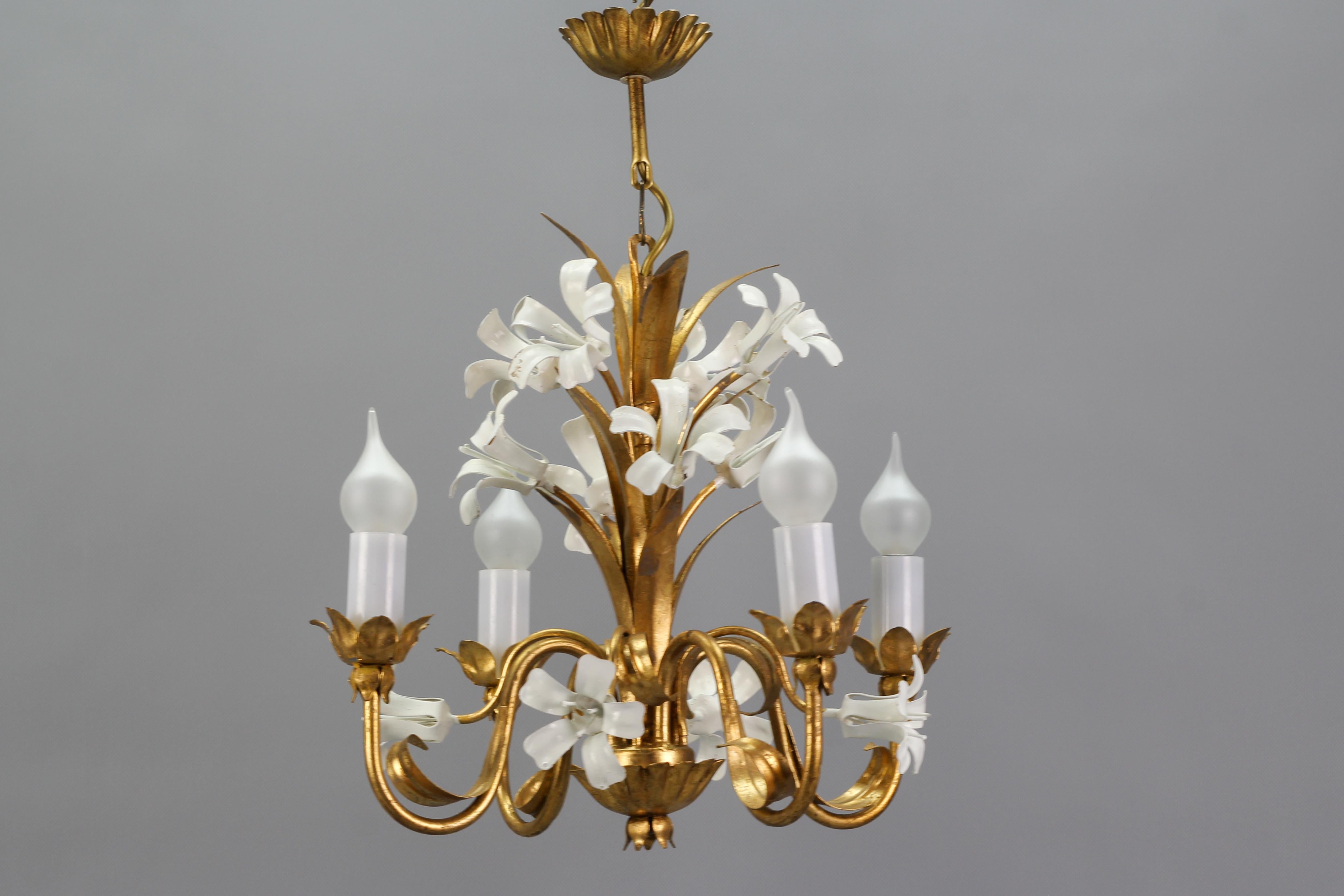 A beautiful Italian gilt metal four-light chandelier from the 1970s. This adorable Hollywood Regency-style golden metal light fixture is adorned with charming flowers - white painted lilies and golden leaves. 
Four sockets for E14-size light
