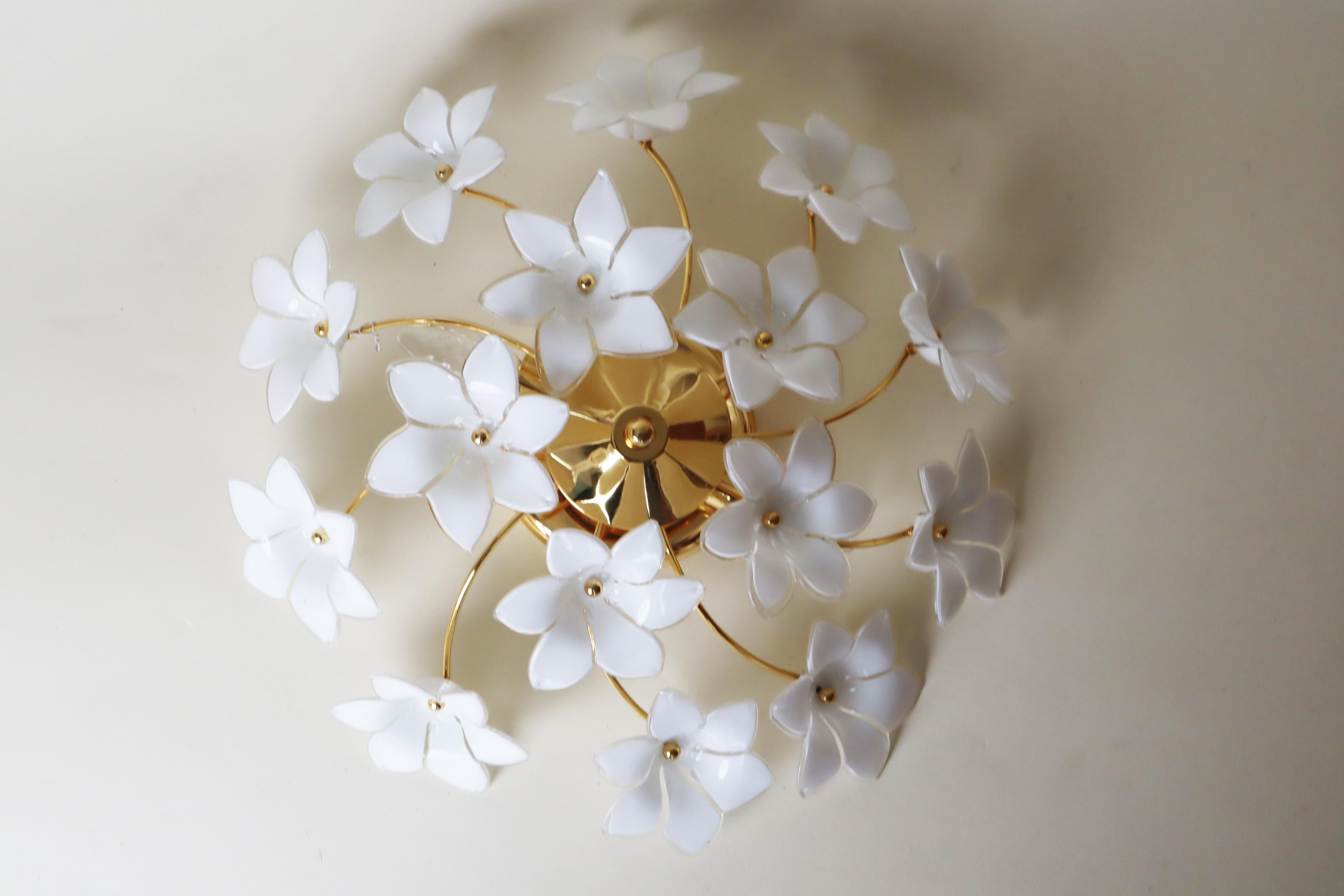 Ce joli plafonnier italien, avec ses fleurs blanches en verre de Murano, a quelque chose de spécial et d'élégant, et émet une belle lumière subtile. Chaque petite fleur de verre est soigneusement fixée au cadre de la lampe dorée à l'aide d'un écrou