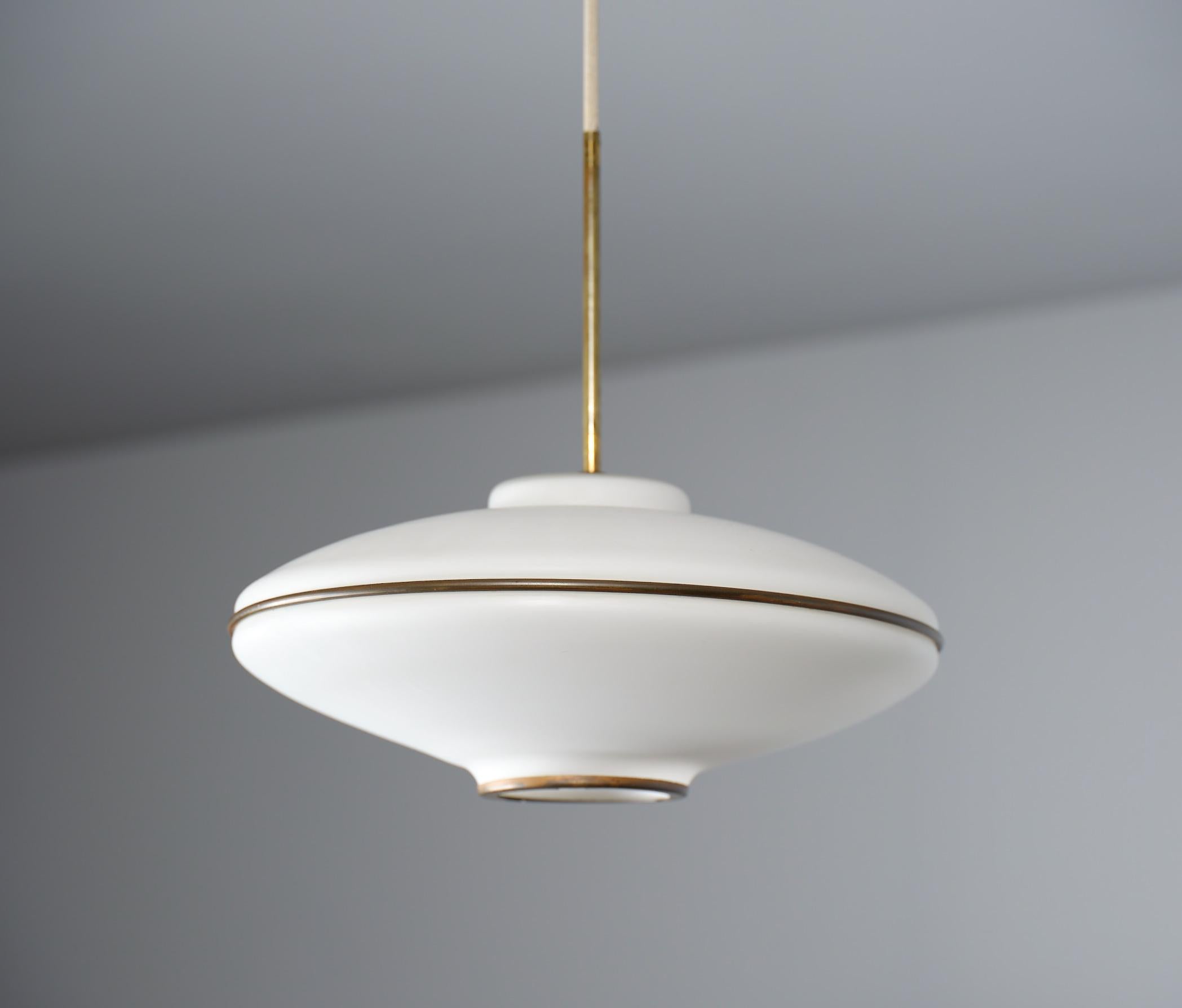  Italian-designed pendant lamp, a timeless piece crafted in Italy during the 1950s. Featuring a sleek modern design reminiscent of a flying saucer, it boasts a large opaline glass shade accented with brass details and cream/beige lacquered metal