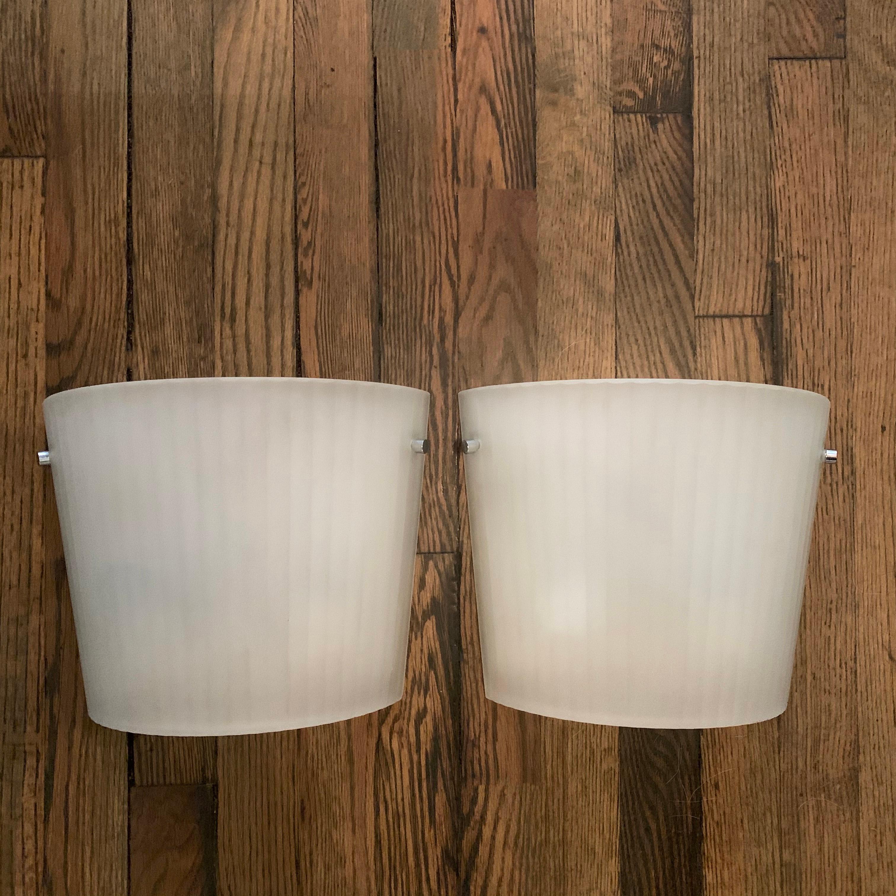 Pair of Italian, fluorescent wall sconce lights by Rodolfo Dordoni for Artemide feature curved, ribbed, frosted glass shades with chrome hardware on metal backplates. The sconces taper in height from 9 - 11 inches.