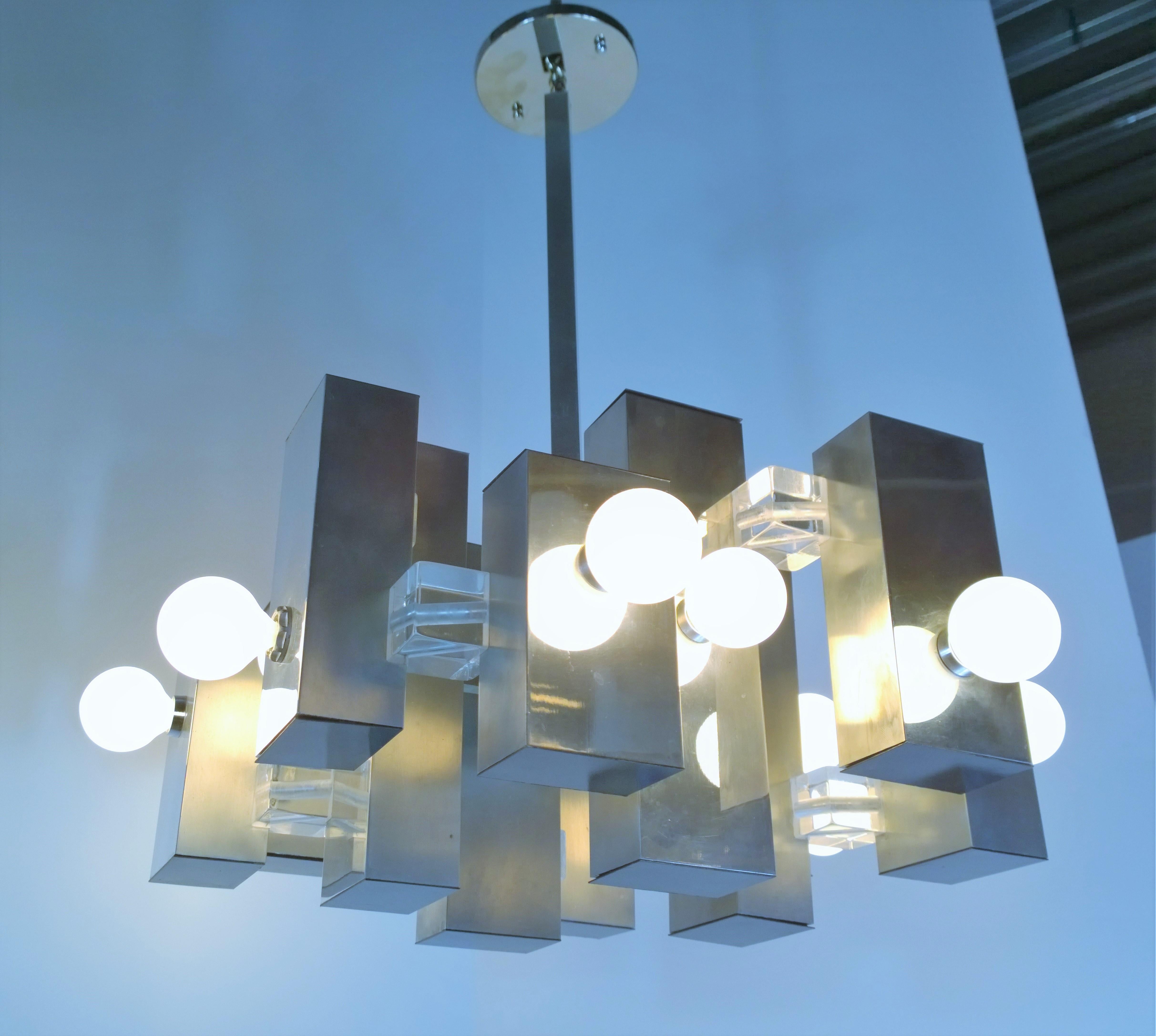 Offered is a Mid-Century Modern Italian Gaetano Sciolari Brutalist chandelier made up of rectangular pieces of stainless steel alternating between mirror finished sides and brushed finished sides capped on tops and bottoms with black painted steel.