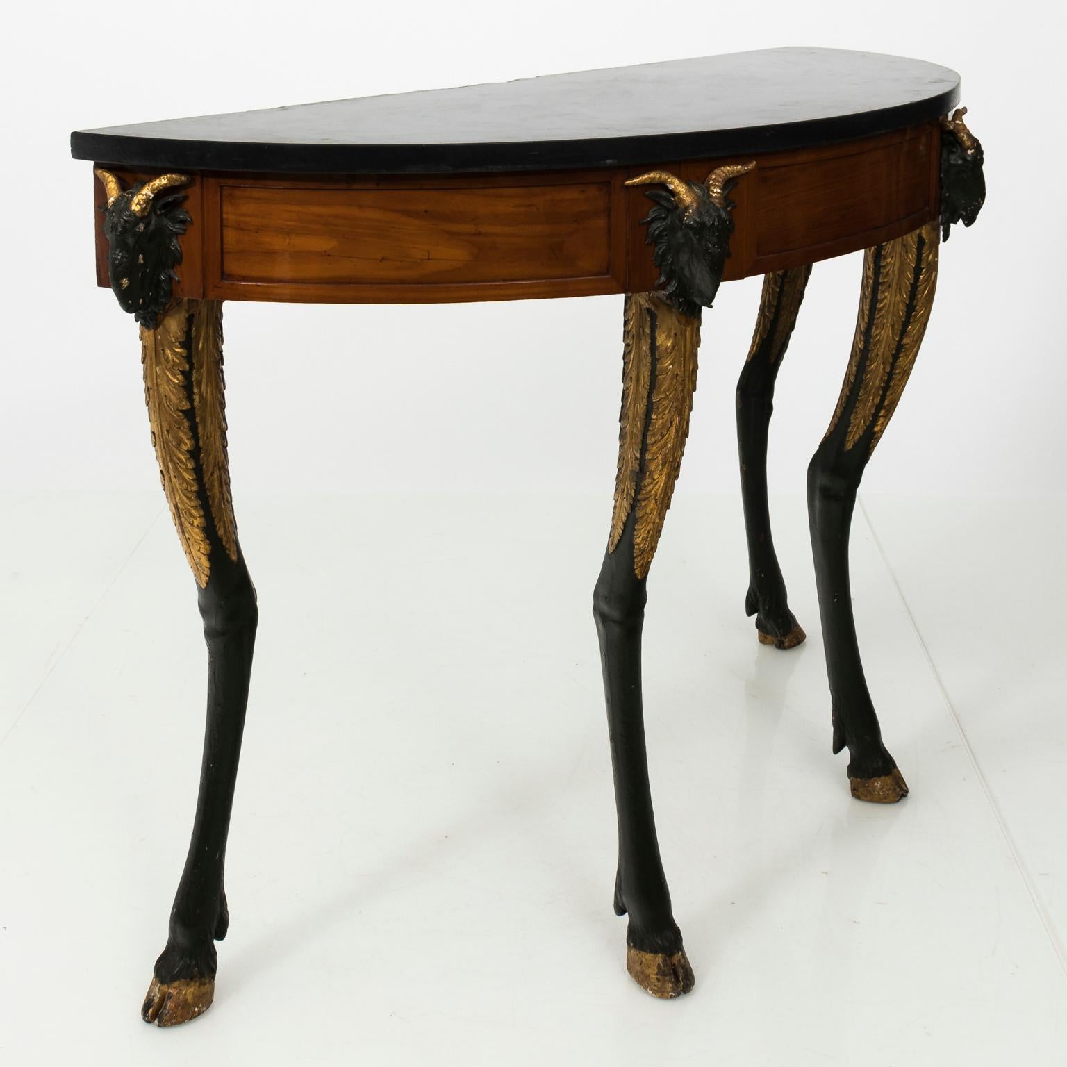 Italian gilded olivewood demilune console table with original black marble top. This table also features black painted ram's heads on the skirt, carved ram's hoof legs, and waterleaves on the knees, circa late 18th century.
 