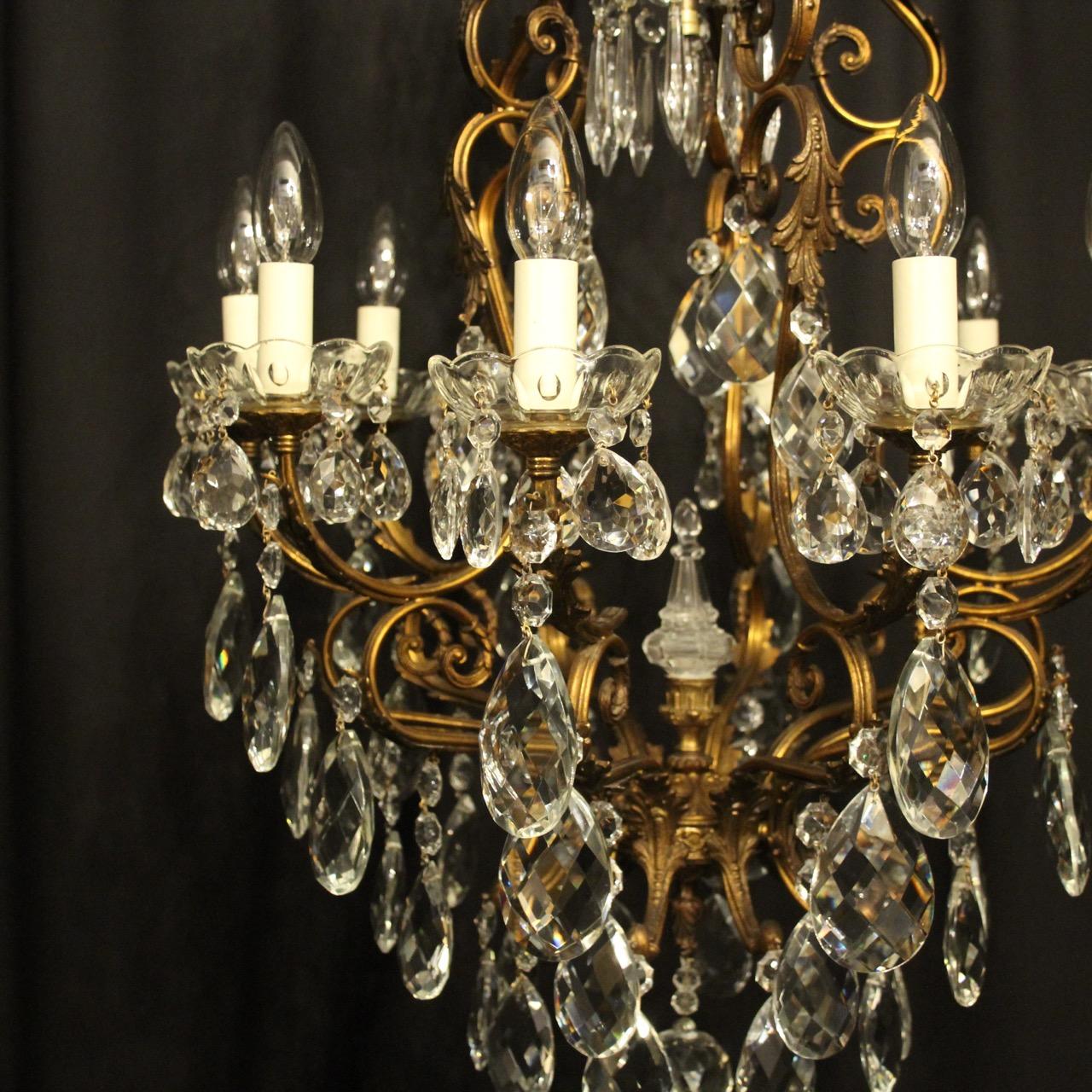 An Italian gilded brass and crystal 11 light birdcage form antique chandelier, the 10 leaf clad scrolling arms with glass bobeche drip pans, issuing from a foliated cage form interior with a single inverted light fitting and prismatic spike,