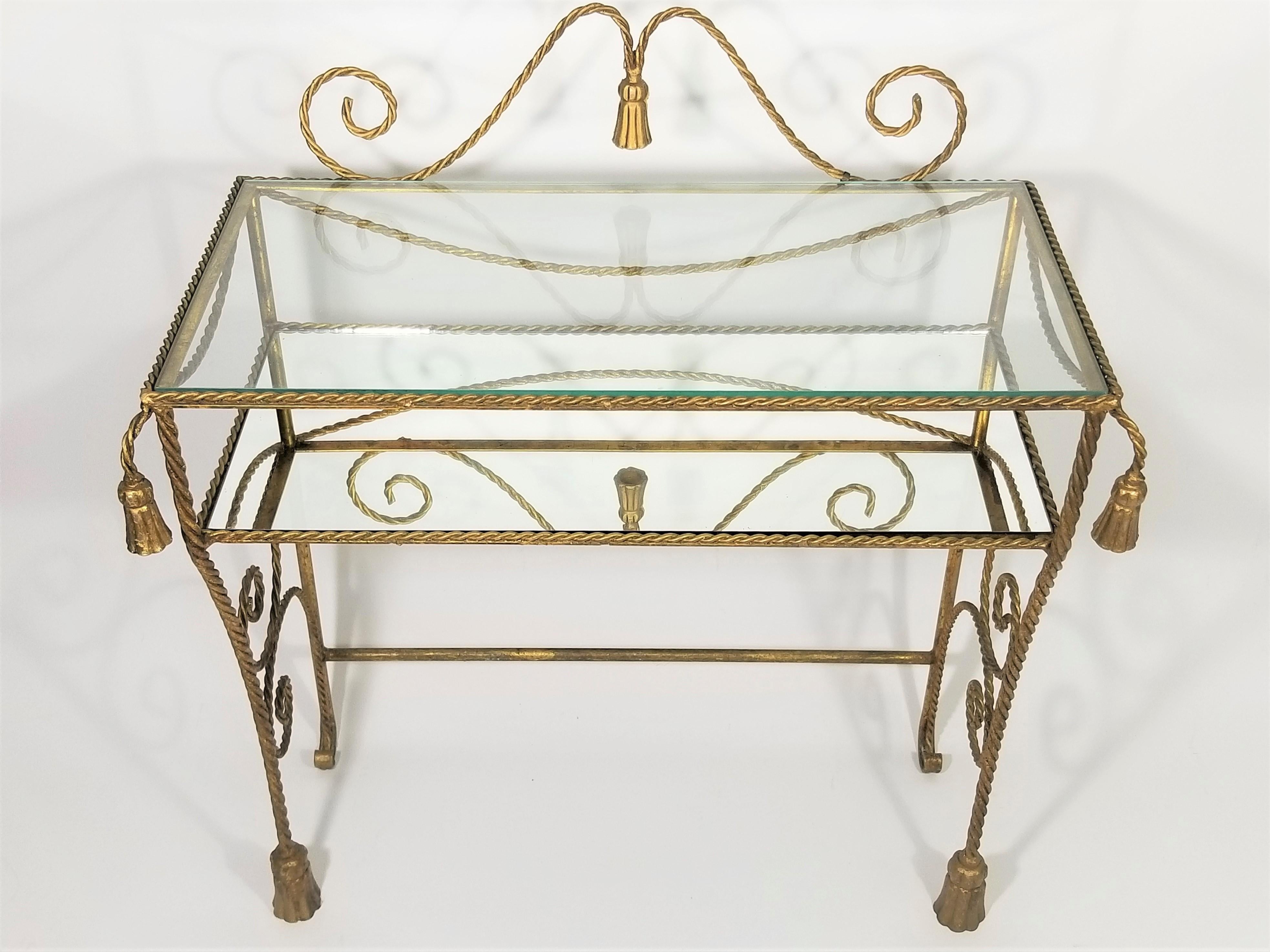 Lovely midcentury 1950s-1960s gilt iron Italian 2-tiered vanity or dressing table. Still retains original metal “Made in Italy” marking tag. Rope and tassel motif. Upper tier is glass and lower tier is a mirror. Petite size would make it ideal for
