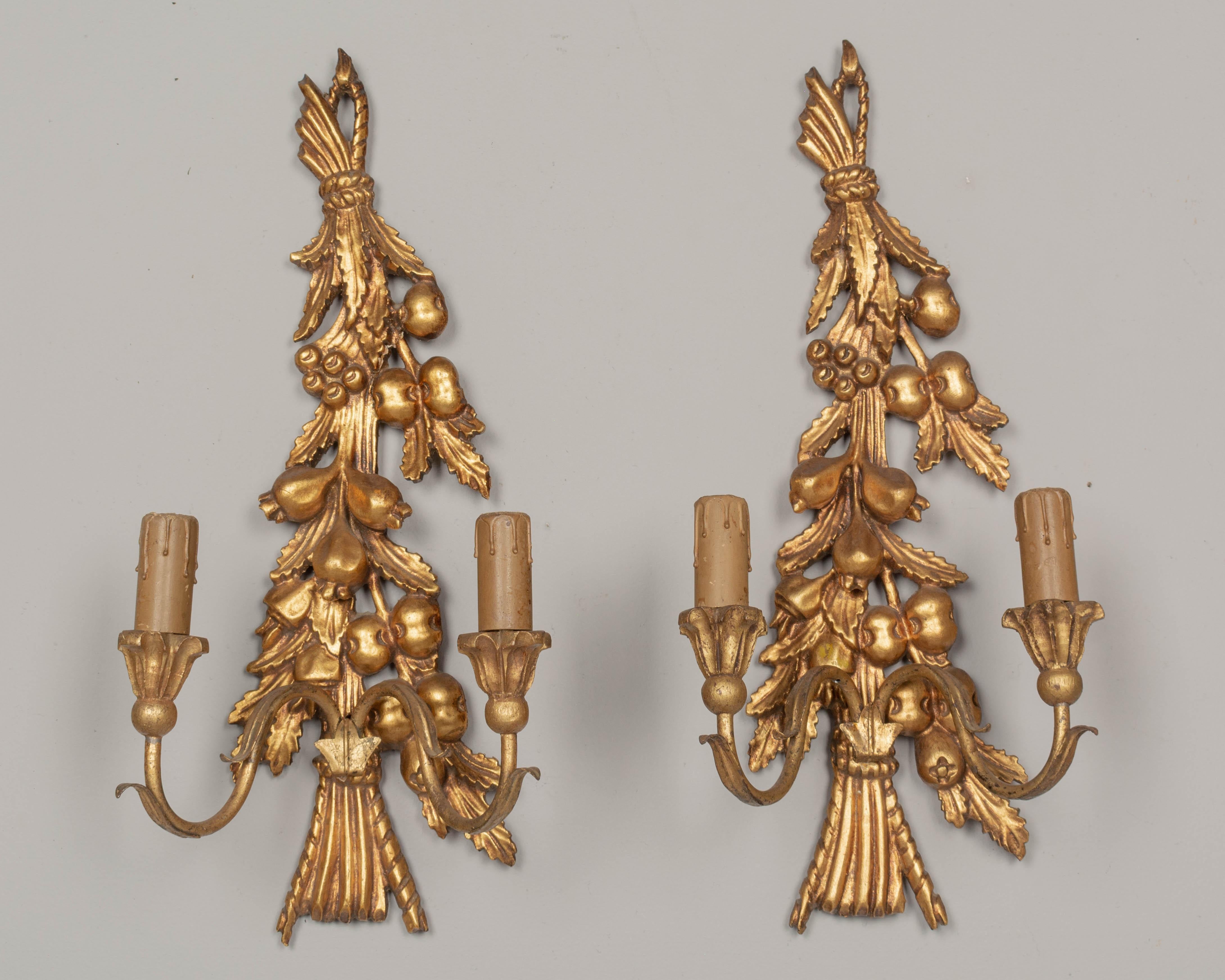 A pair of Italian two-light carved and gilded sconces with tole leaves. Nice three dimensional detail of pomegranate fruits and leaves. In good condition with bright gilt. Original candle covers. Rewired with new sockets. Minor restoration.
 