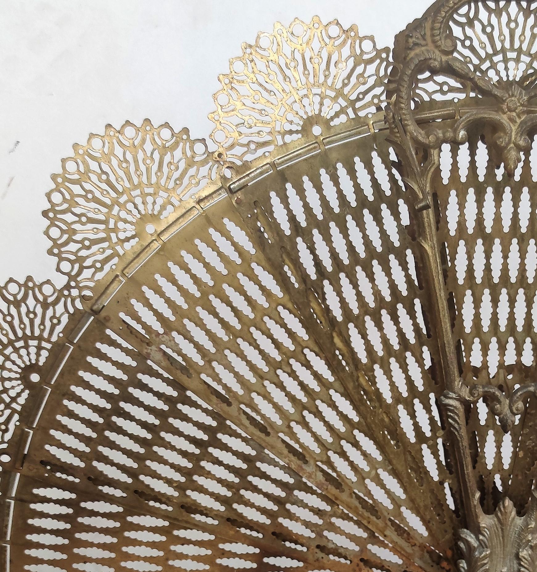 Italian gilt brass decorative pierced in a peacock fan design folding fire place fan screen 
with a foliage and berry handle, intertwined scrolled floral swags with a floral medallion, centered supporting bead work, and resting on a step back