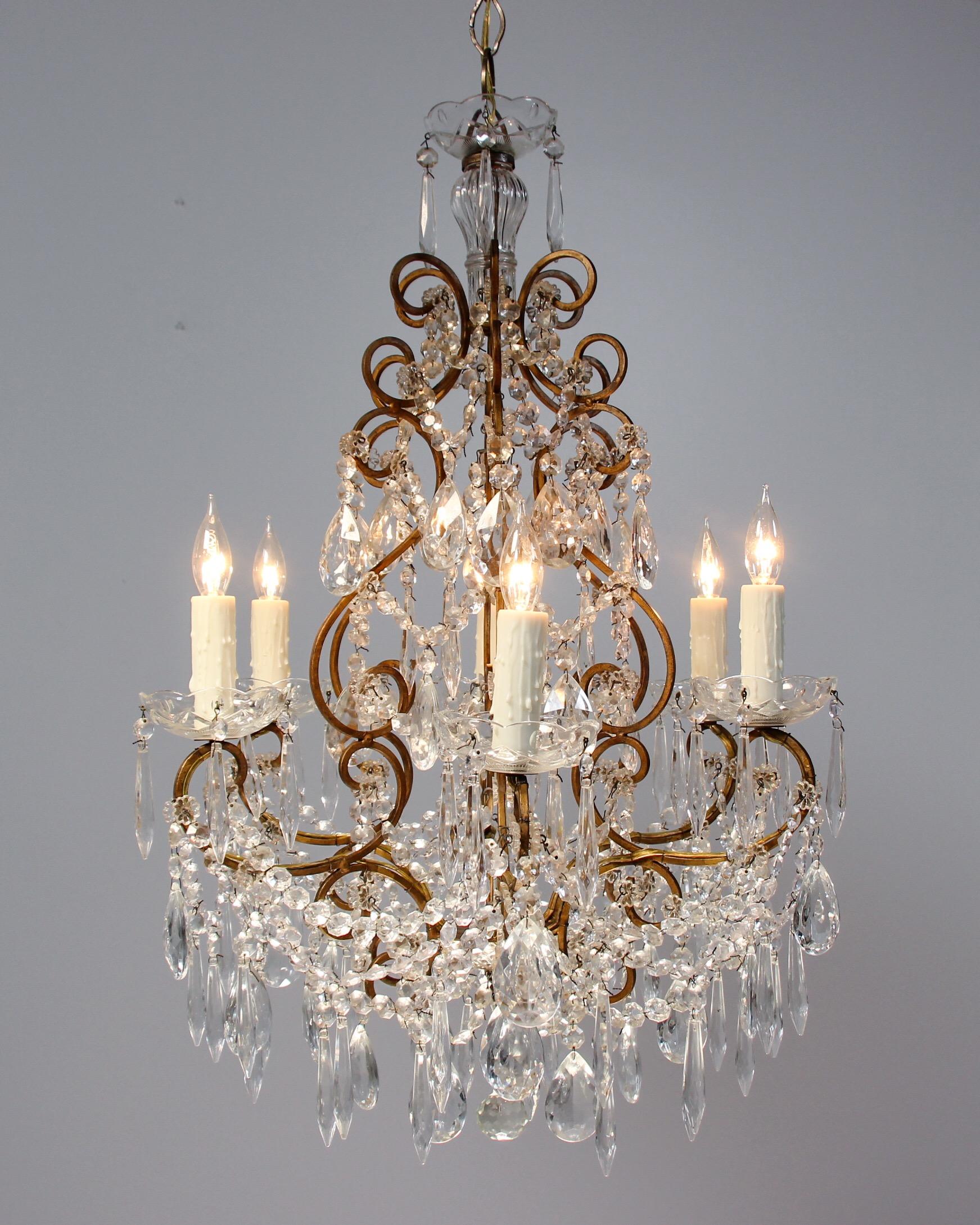      Elegant, 1950s Italian chandelier featuring a scrolly gilt-iron frame generously decorated with crystal prisms and garlands. 
     Substantial in appearance, the chandelier would accent any space nicely. 
     Wired and in working condition.