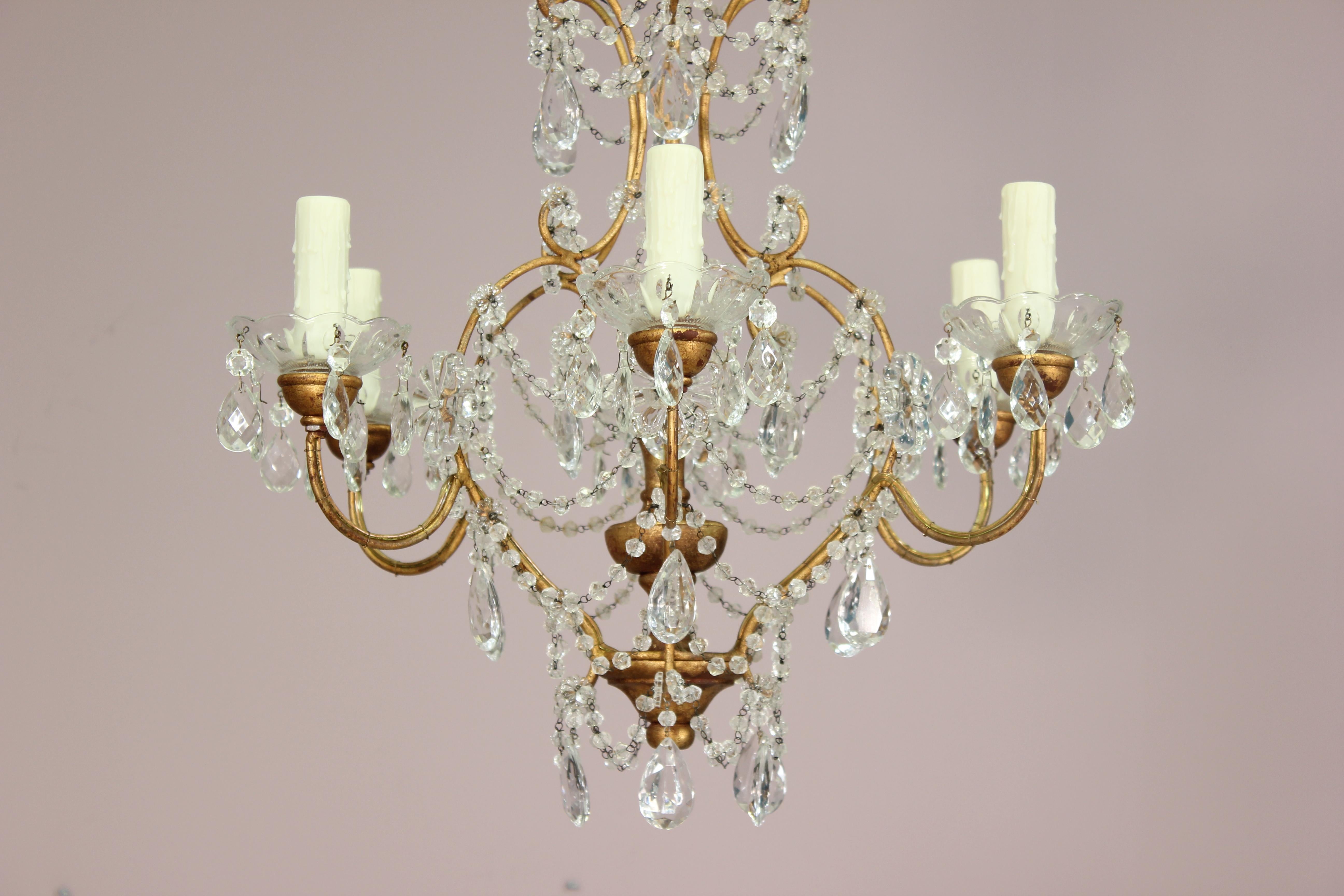Charming Italian gilt iron crystal chandelier with giltwood accents in the Rococo style. The chandelier features a delicately shaped gilded iron frame which is decorated with garlands of English cut beads and faceted prisms. 
Wired and in working