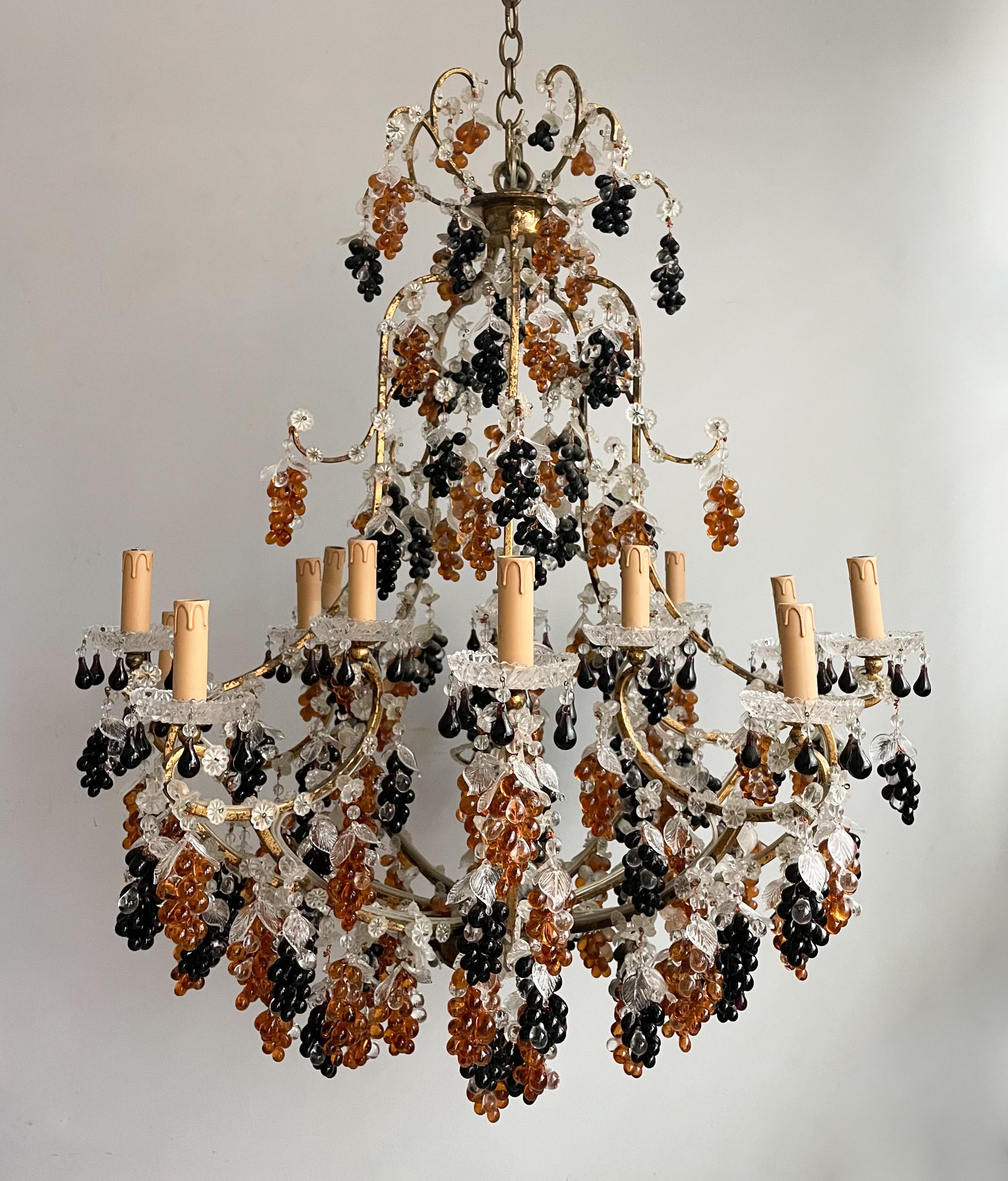 Gorgeous, vintage Italian gilt-iron chandelier in the provincial style. 

The chandelier consists of a multi-tiered, gracefully scrolled iron frame in hand-applied tarnished gold leaf finish. An abundance of Murano glass grape clusters in amber and