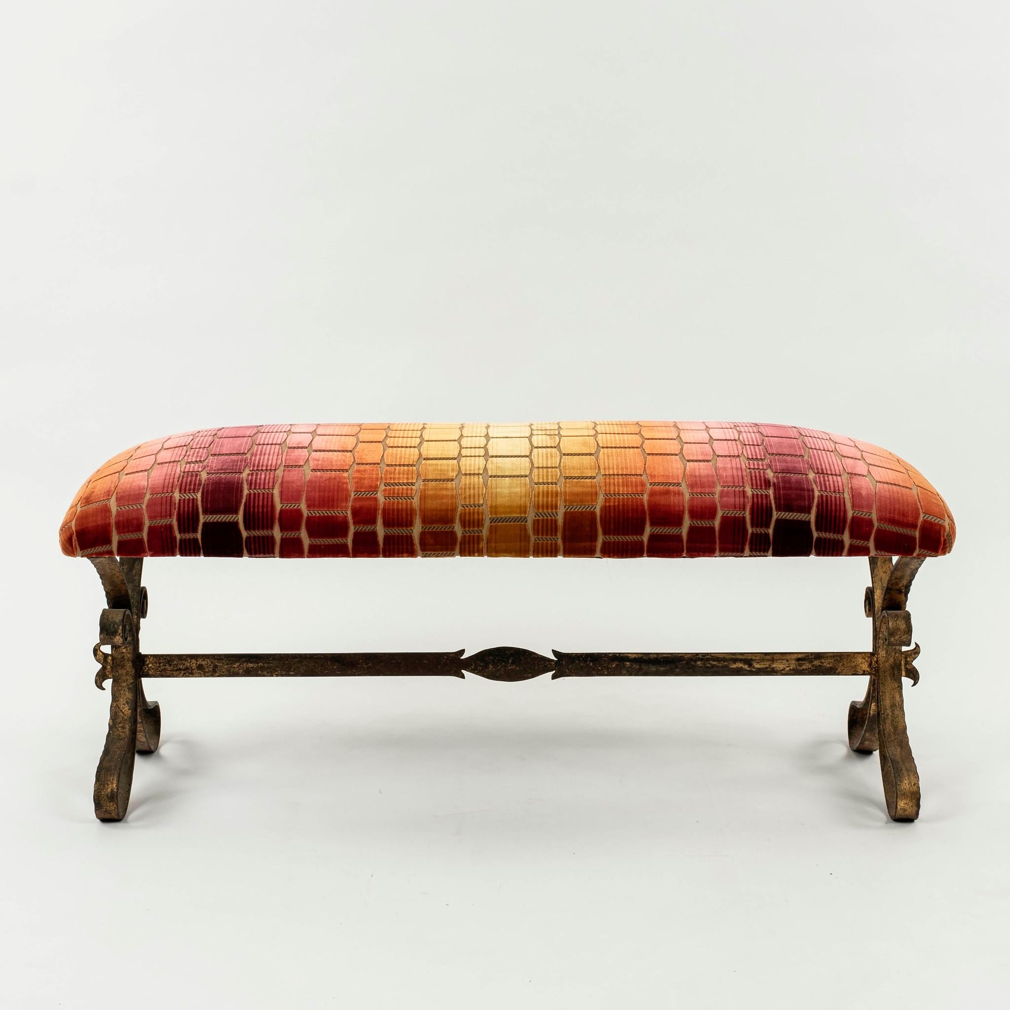 Italian gilt iron bench upholstered in a geometric cut velvet with undulating hues of yellow, pink, and red tones.