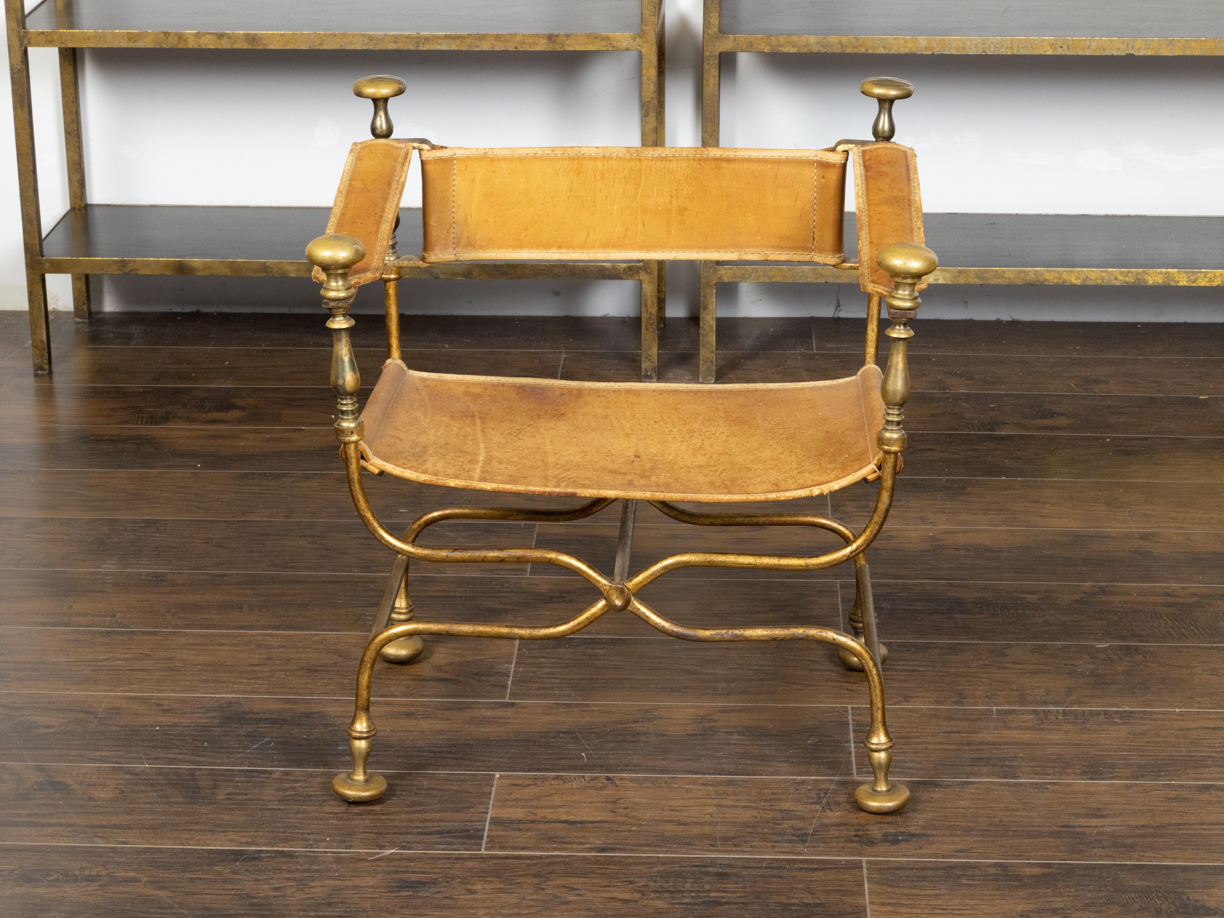 An Italian vintage gilt iron Savonarola curule armchair from the mid 20th century, with leather seat, flattened finials and X-Form base. Created in Italy during the Midcentury period, this Savonarola chair features a gilt iron structure with a shape