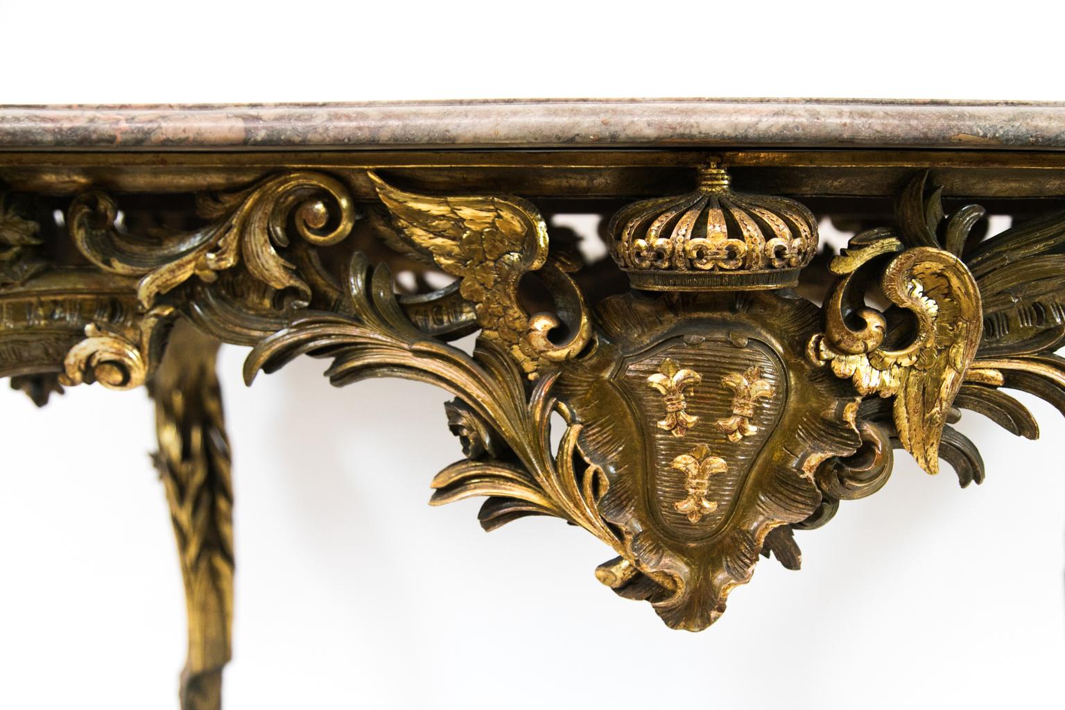 Italian gilt marble top center table has a serpentine molded edge on all four sides with ovolo corners. The carved cabriole legs have three dimensional open work leaf carvings. The apron has a carved gilt crown atop a cartouche with three carved