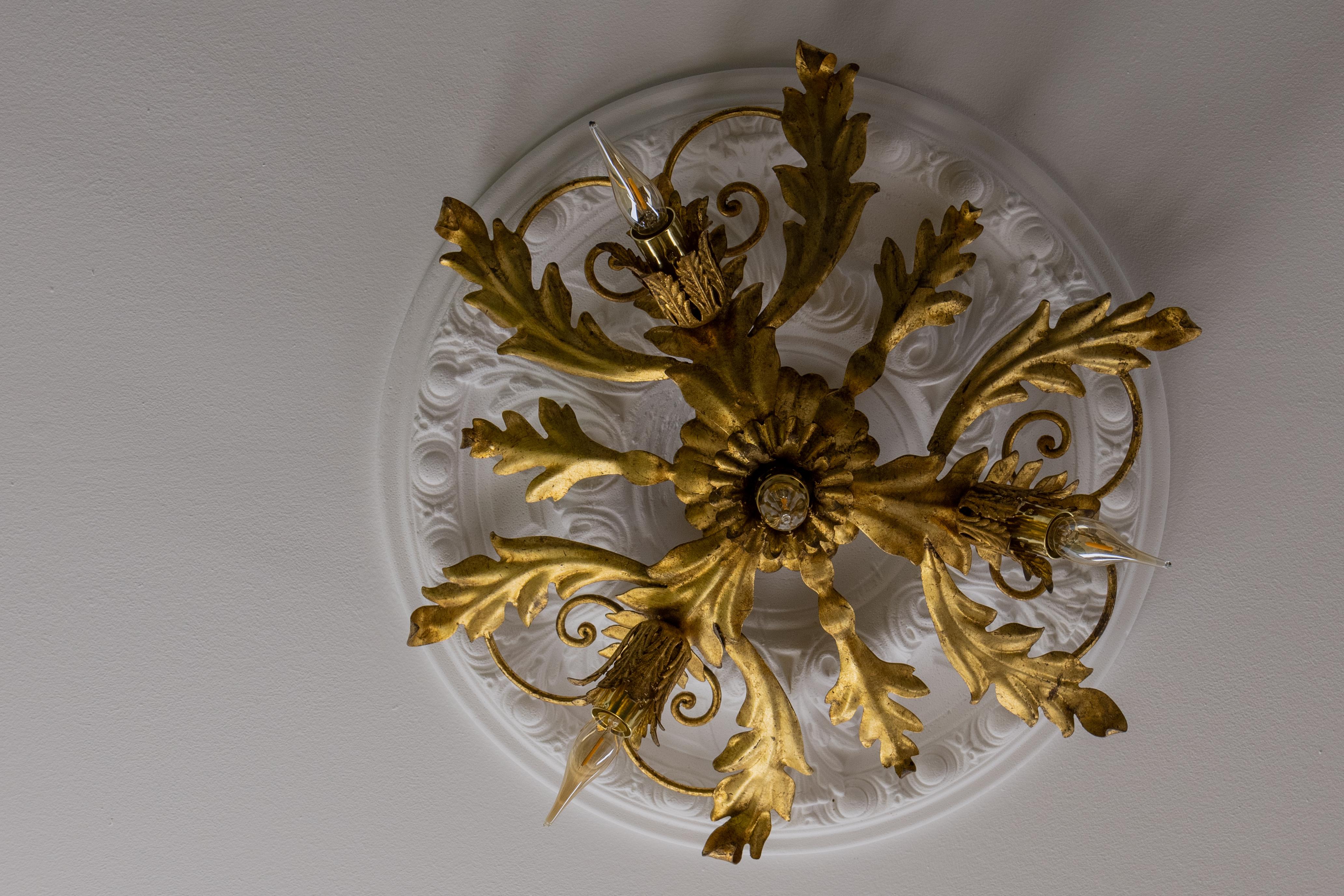 Lámpara de techo de cuatro luces de metal dorado de la Regencia de Hollywood italiana de los años 70, con detalles foliados.

Esta lámpara de techo decorativa, fabricada en Italia en la década de 1970, refleja el estilo opulento de la Regencia de