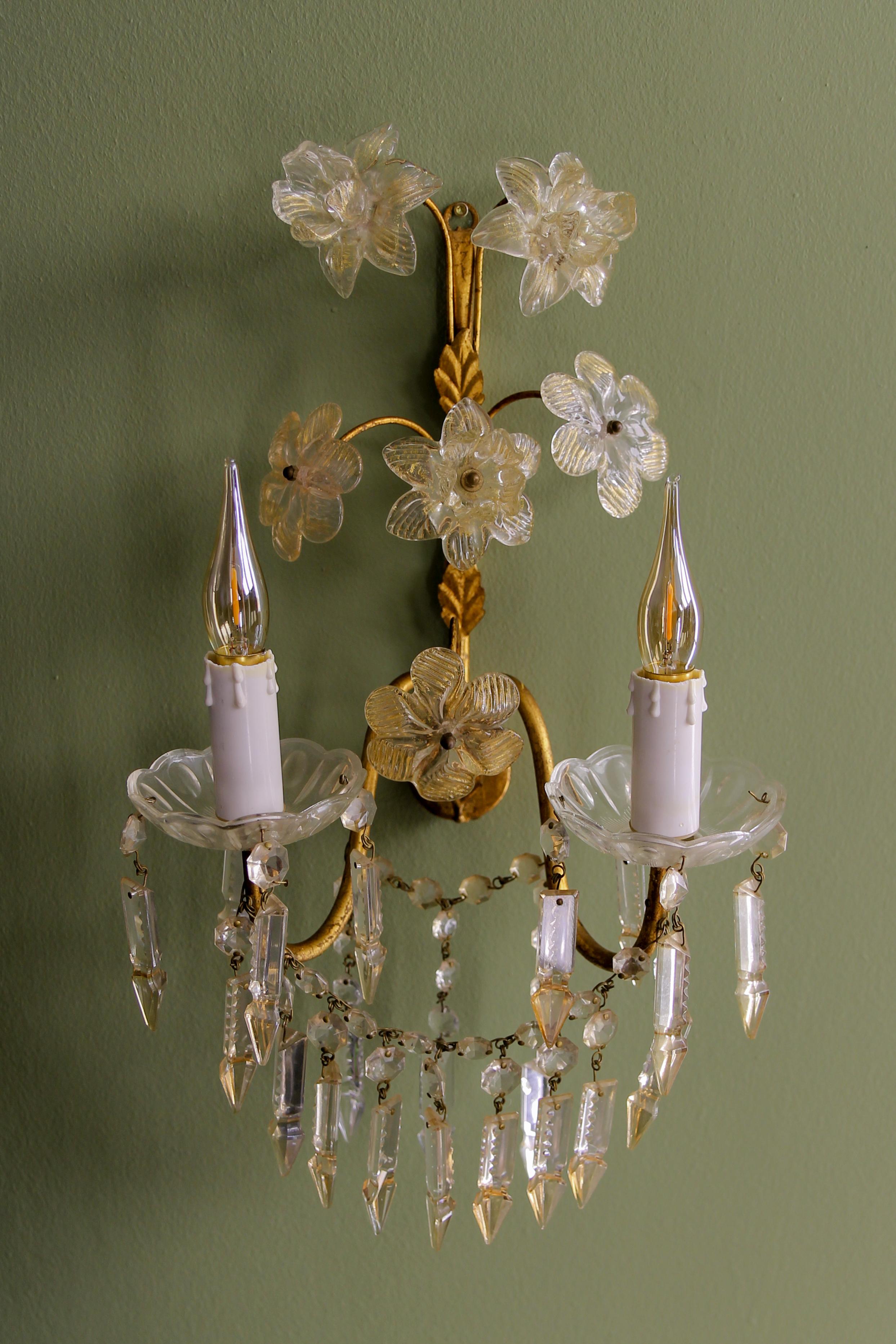 Italian gilt metal two-light sconce with crystal glass flowers and prisms, circa the 1970s.
This beautiful wall lamp features a gilt metal frame with leaves and two arms, each with a glass bobeche and a socket for an E14-size light bulb. This