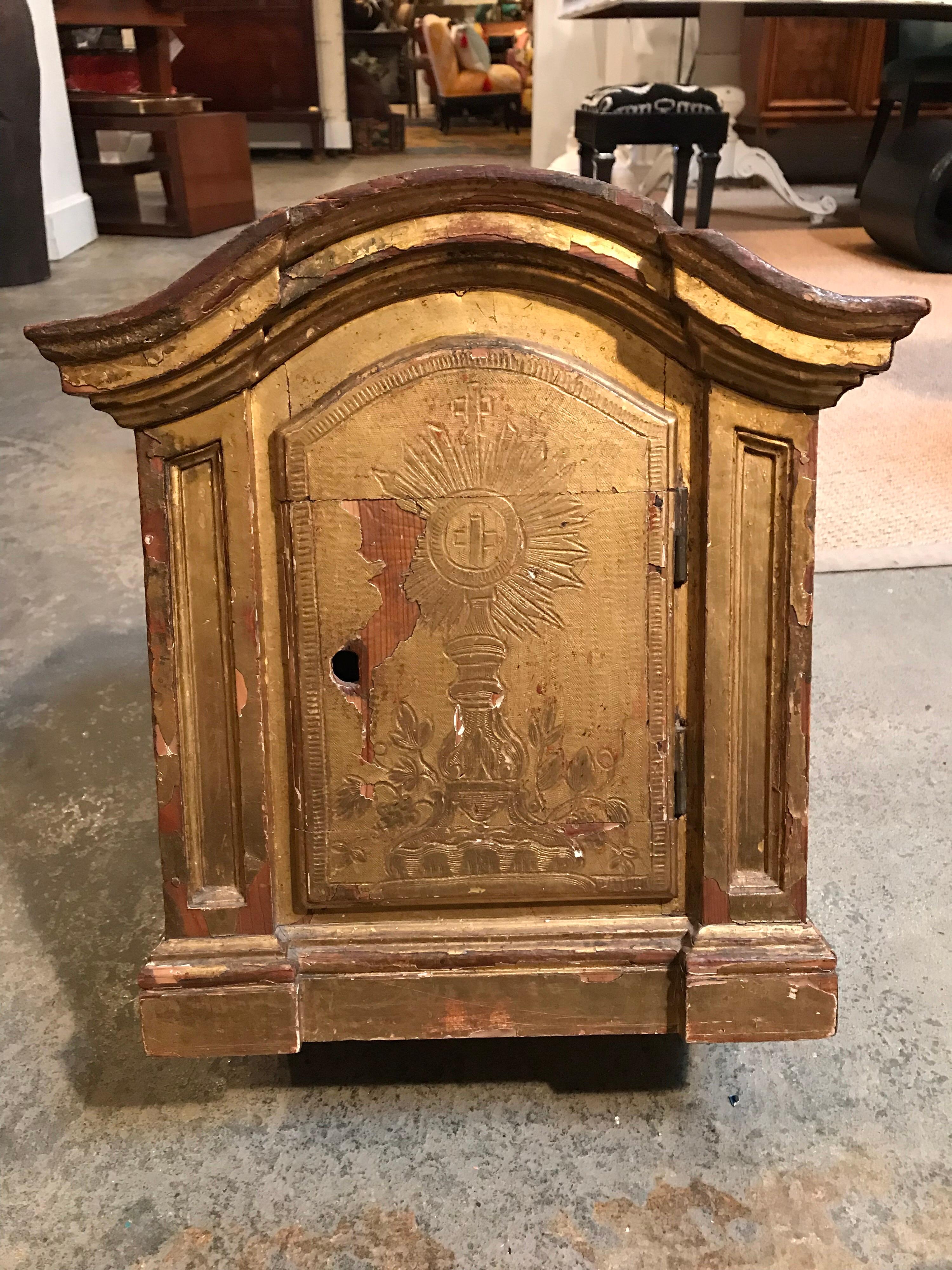 This 18th century Italian gilded reliquary box is made to contain a personal relic or shine. It has brackets for wall mounting. The front of the door has a hand carved image of such a shrine with a cross in the center.