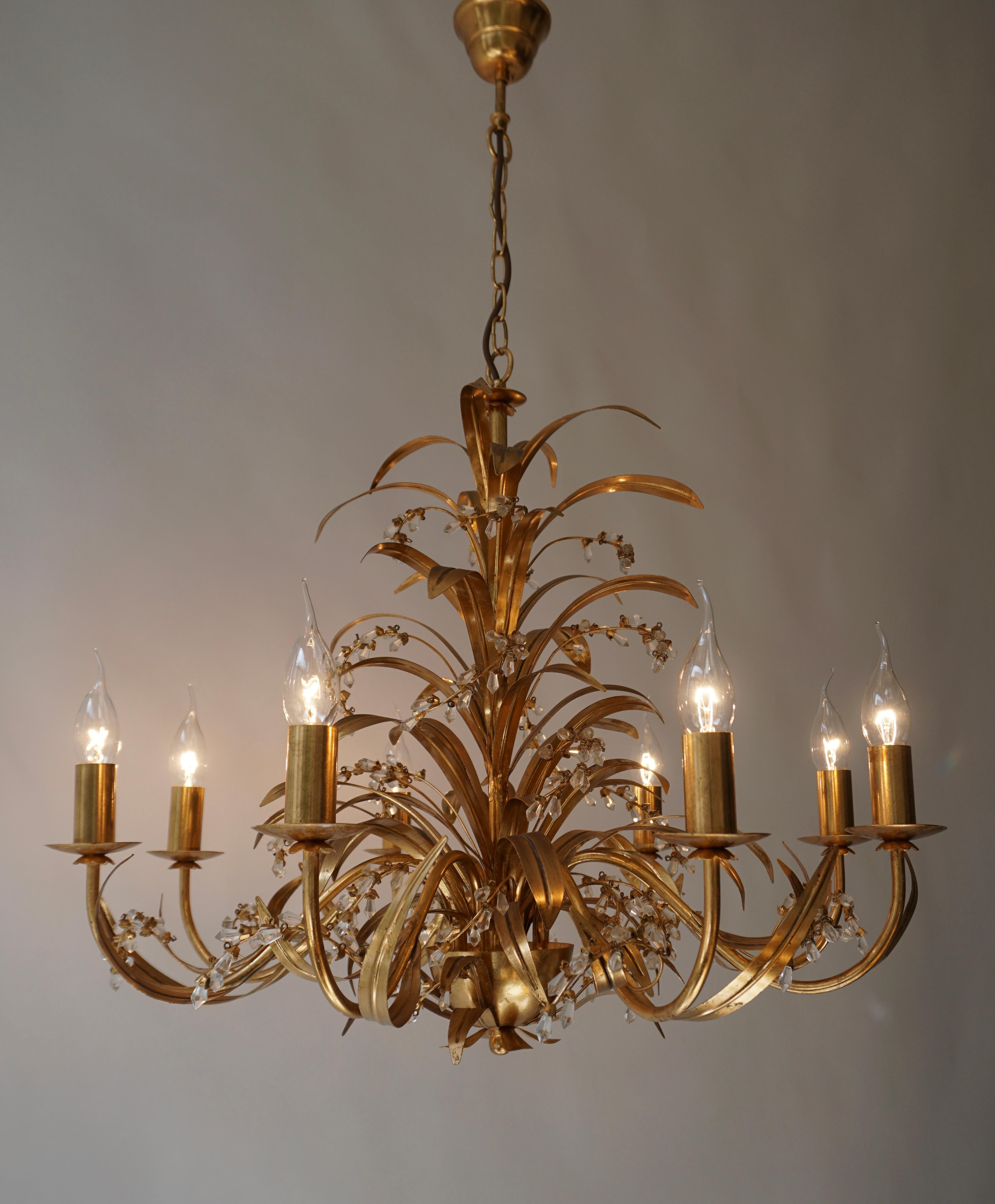 A Hollywood Regency style five-light gilt metal chandelier with tôle palm fronds and crystal glass decoration. Attributed to Hans Kögl and made in Italy. Original candle covers and canopy. In working order. Very good original vintage condition.