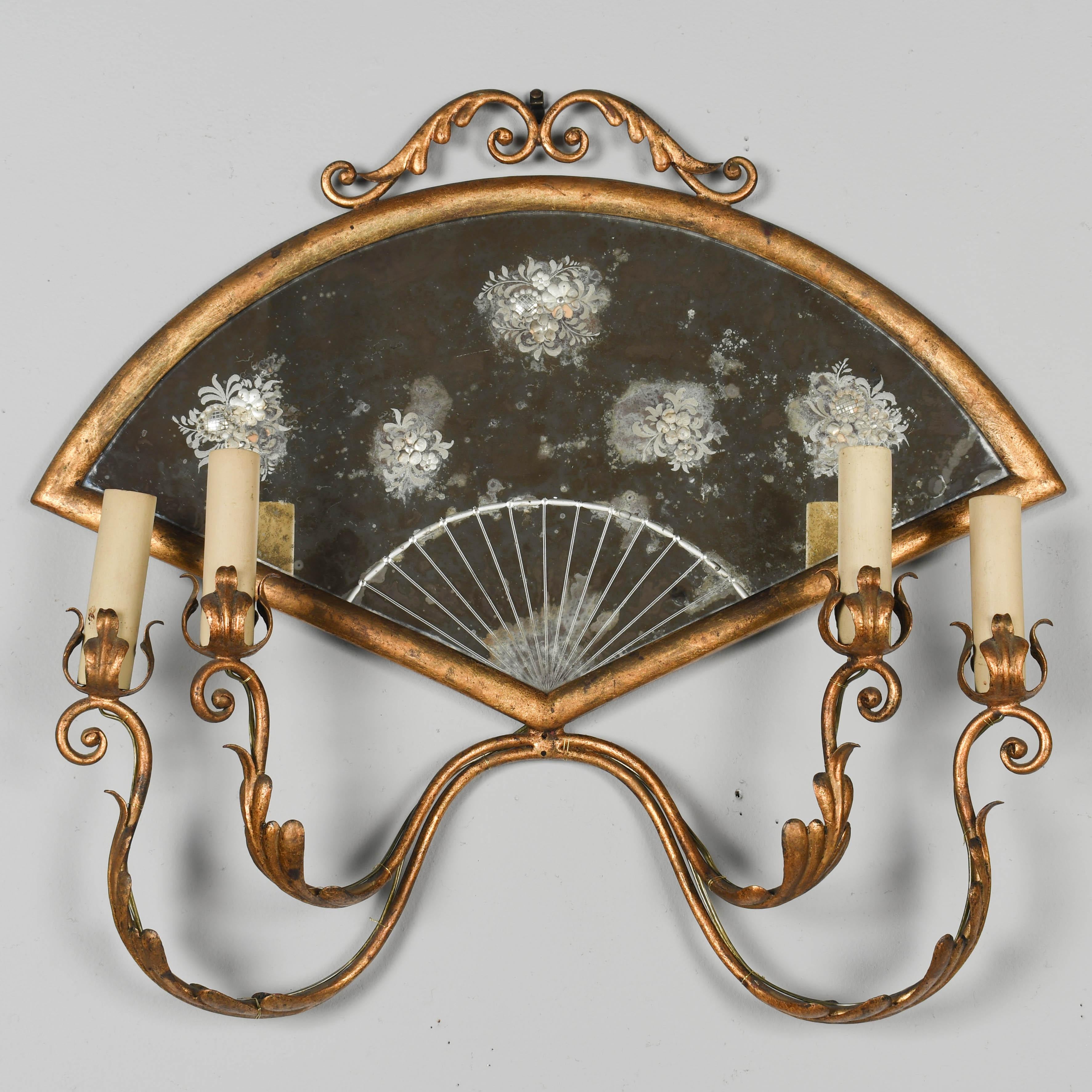 Applique murale italienne en fer doré à quatre lumières avec une grande plaque arrière en miroir gravé en forme d'éventail. Bras à volutes avec décor de tôles feuillagées dorées. Recâblage avec prises d'origine et adaptateurs USA. Couvercles de